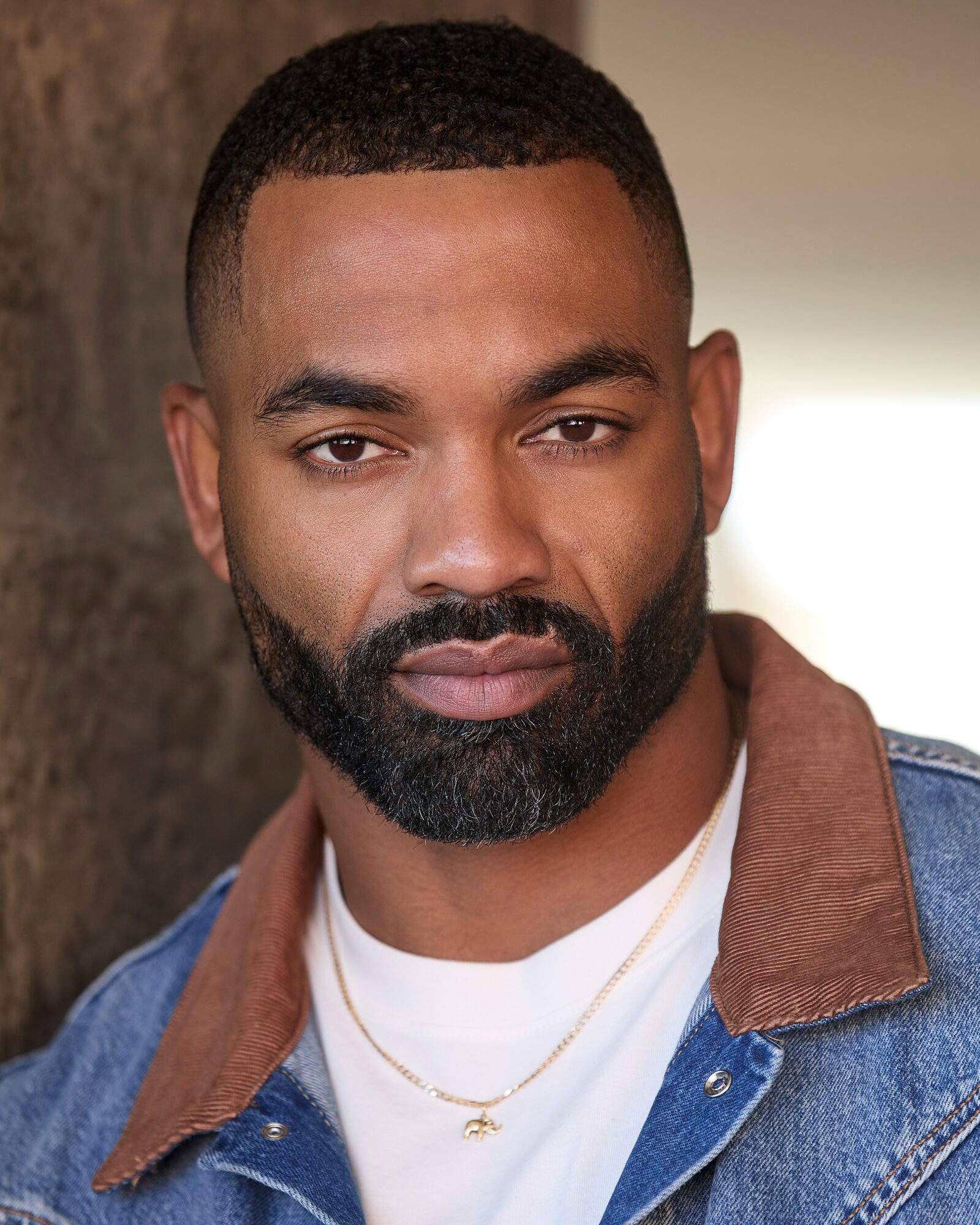 Portrait of a man with short hair and a beard, wearing a denim jacket with a brown collar and a white shirt.