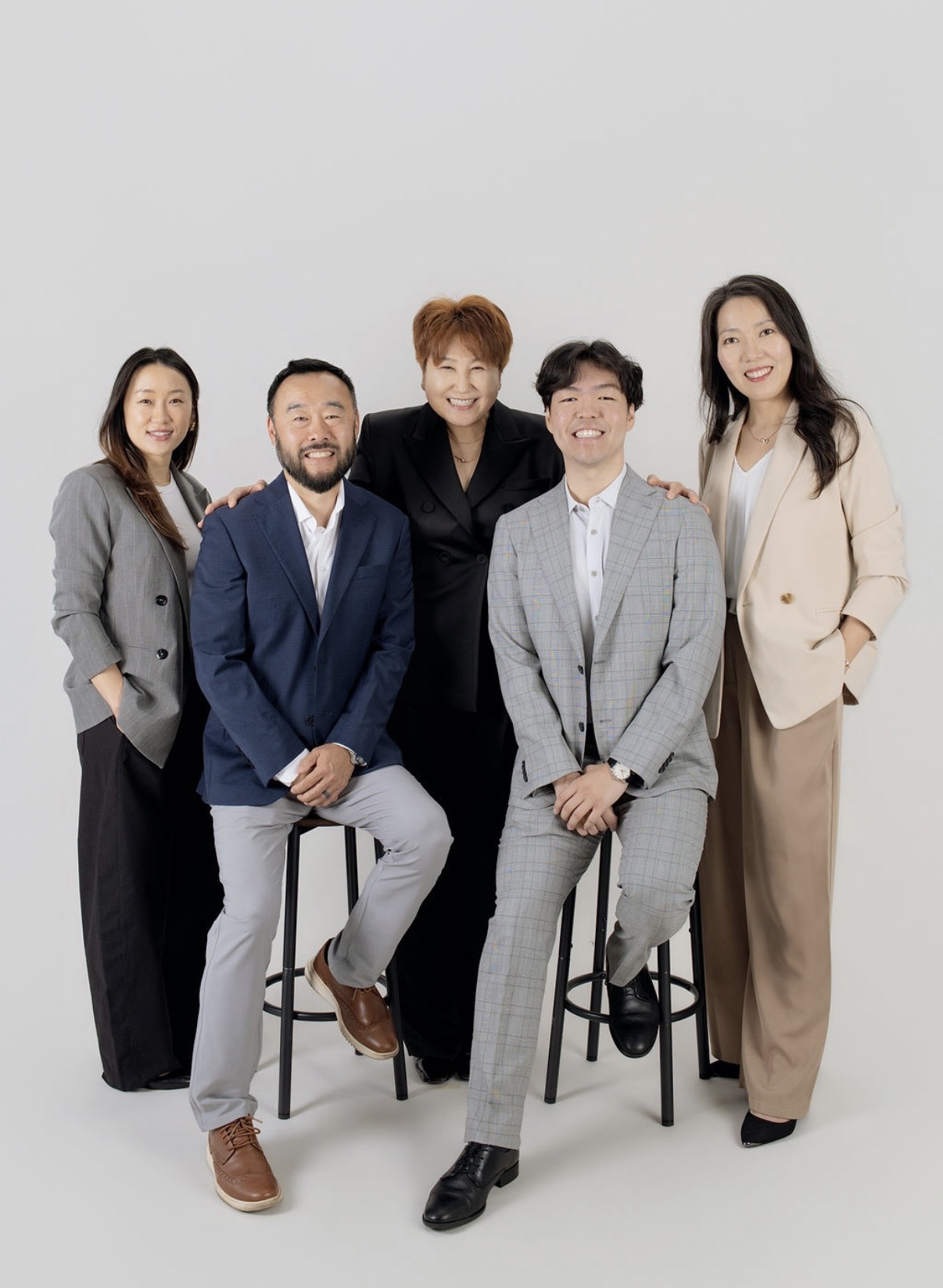 Group of five people, three men and two women, standing and sitting against a plain white background.