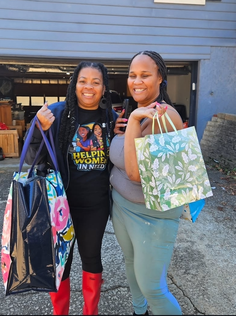 Two women smiling and holding shopping bags outdoors, standing in front of a blue building.