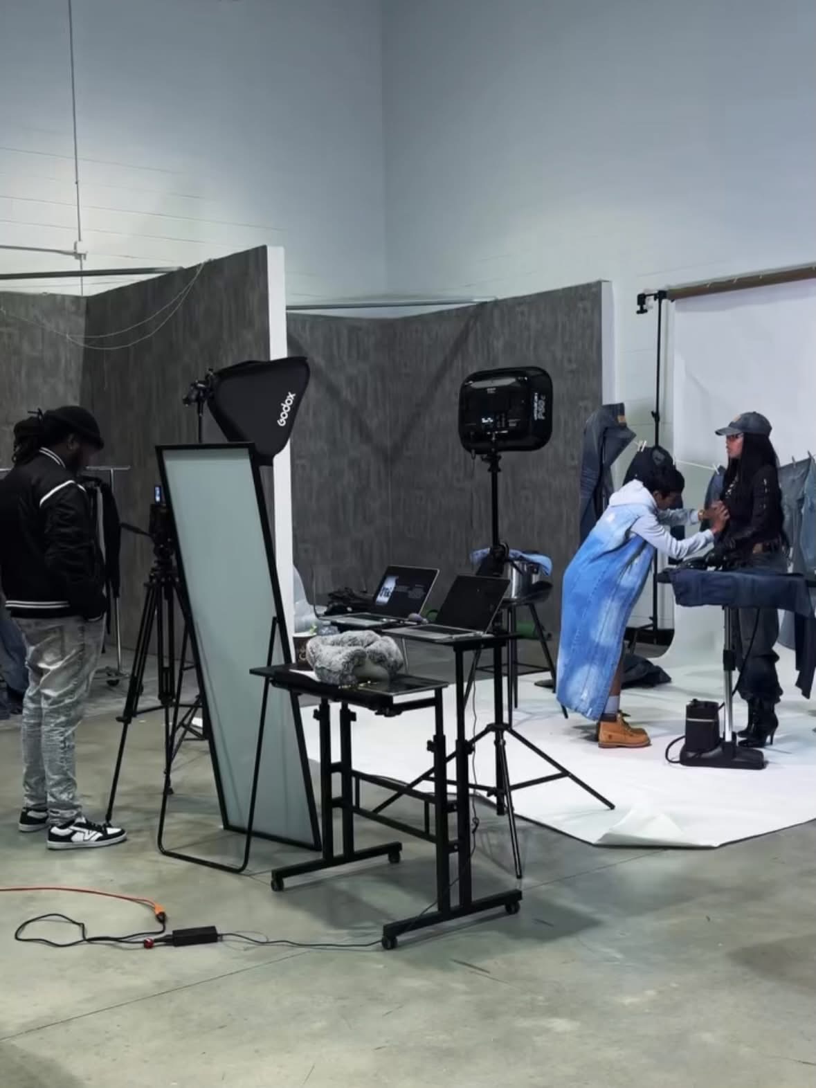 People in a photography studio with lighting equipment and a backdrop, some working at a table, others standing nearby.