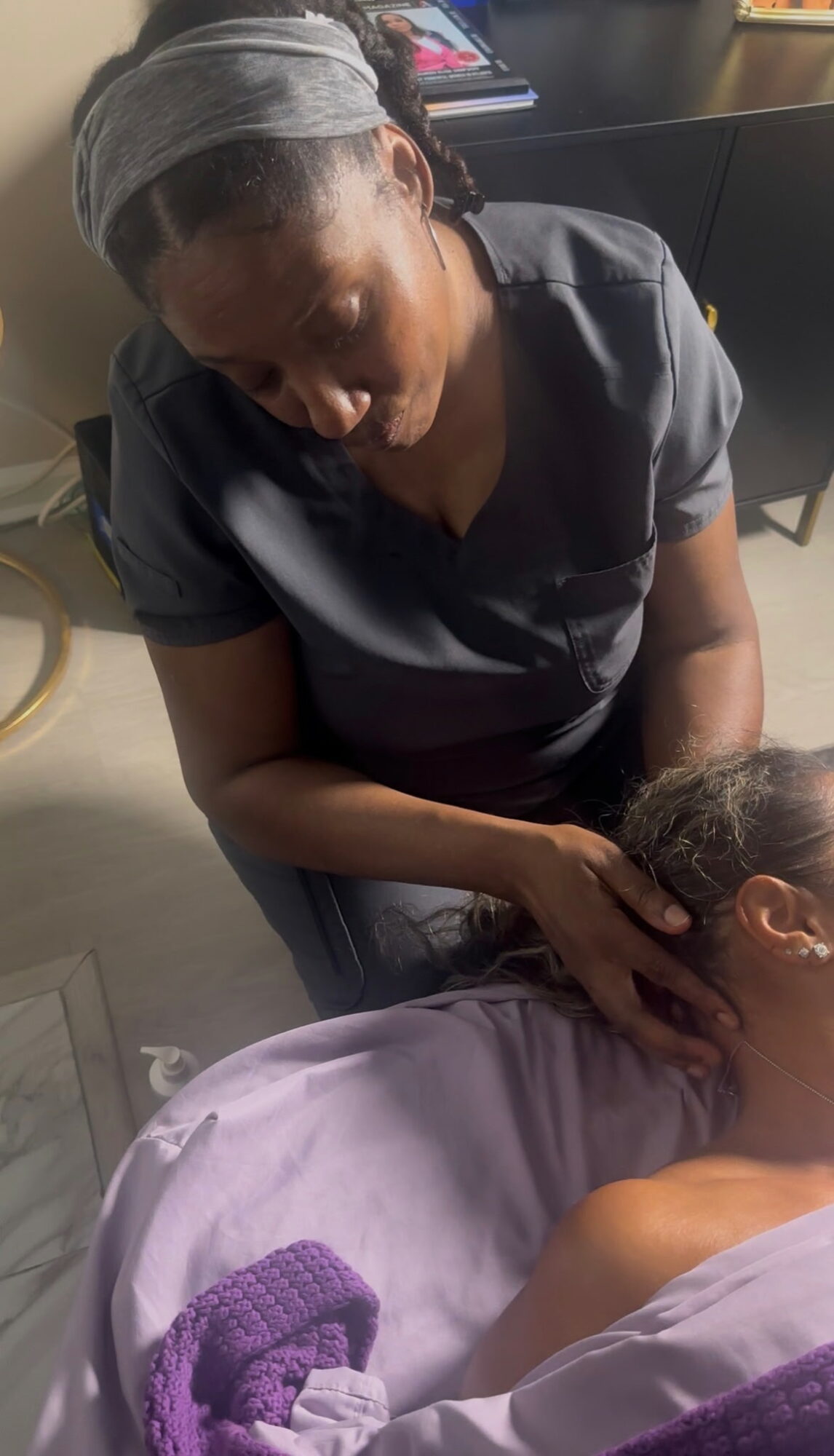 A person providing a massage or treatment to another person lying down, in a professional setting.