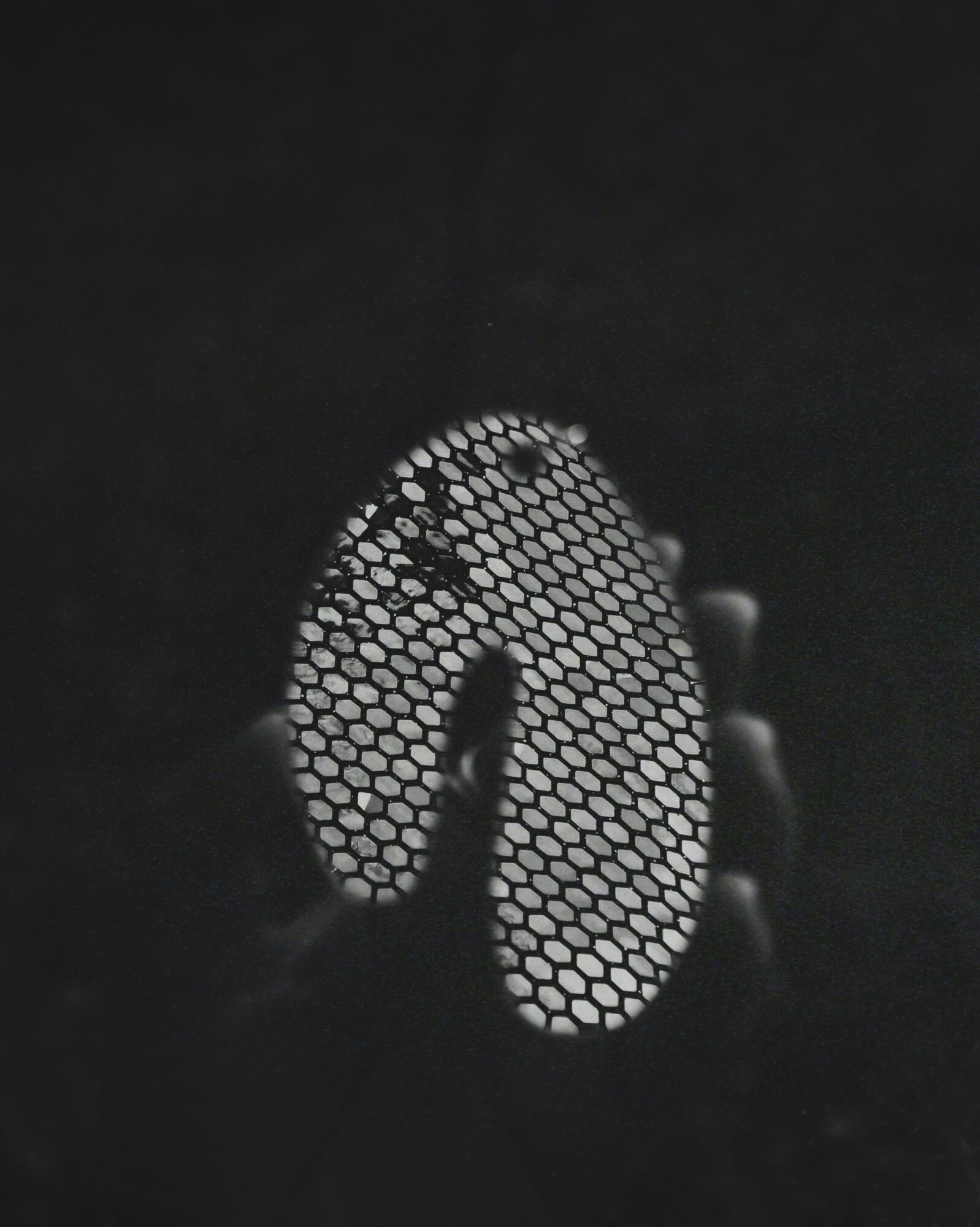 Hand holding a circular object with a honeycomb pattern, against a dark background.
