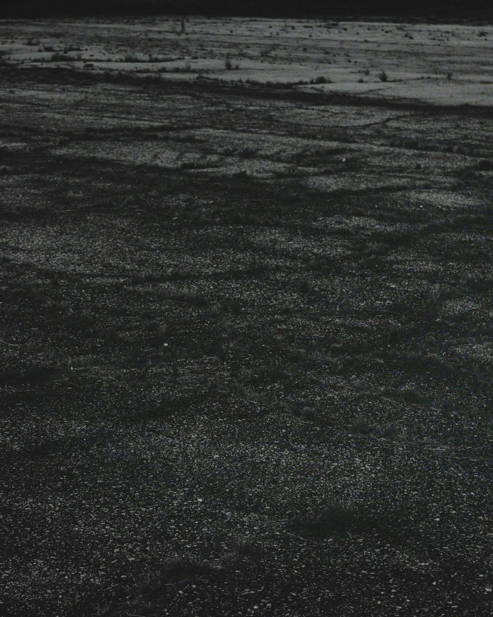 Dark, textured landscape with a flat, barren surface and distant horizon, under a dark sky.