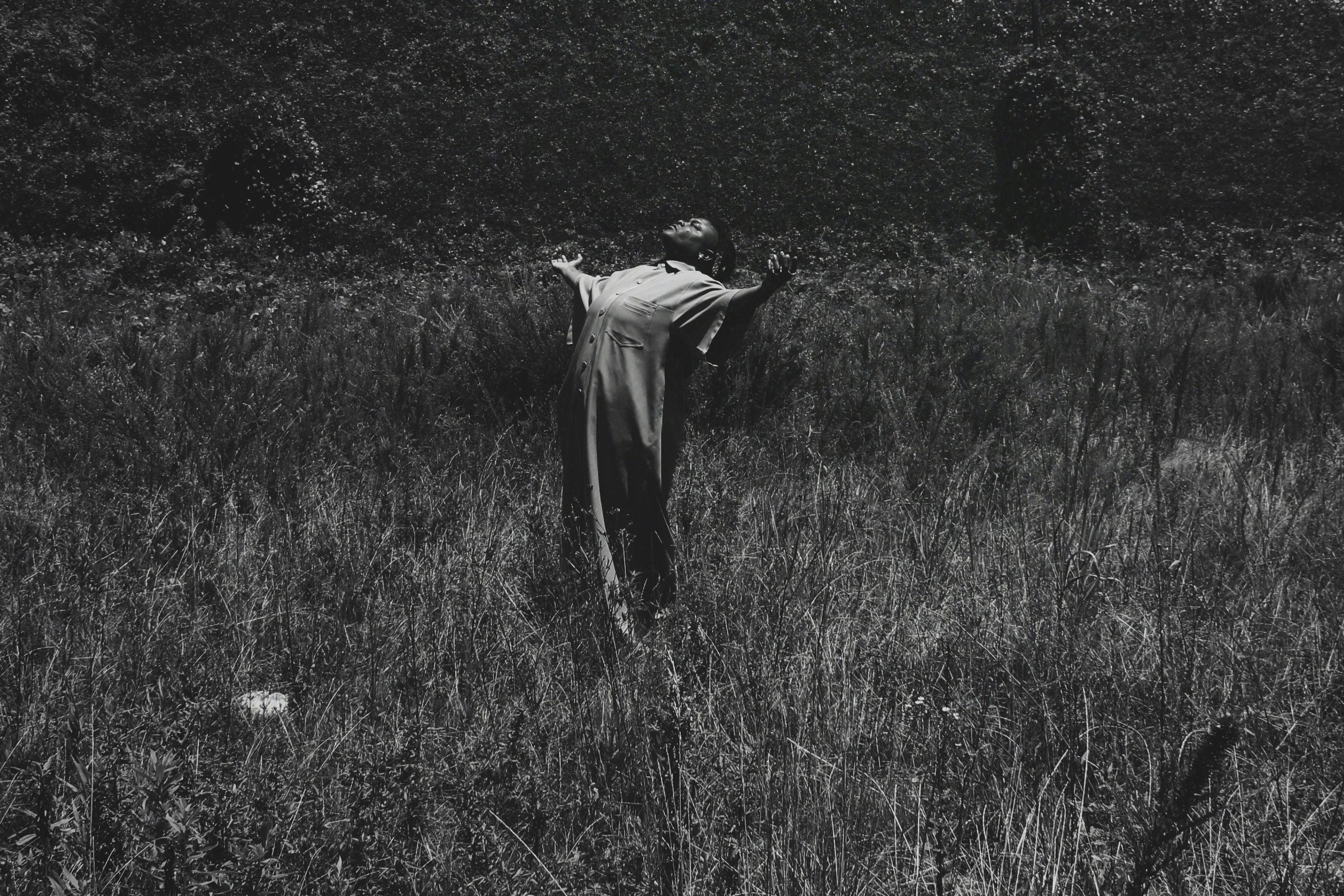 Person standing in a grassy field with arms raised, facing away from the camera, in black and white.