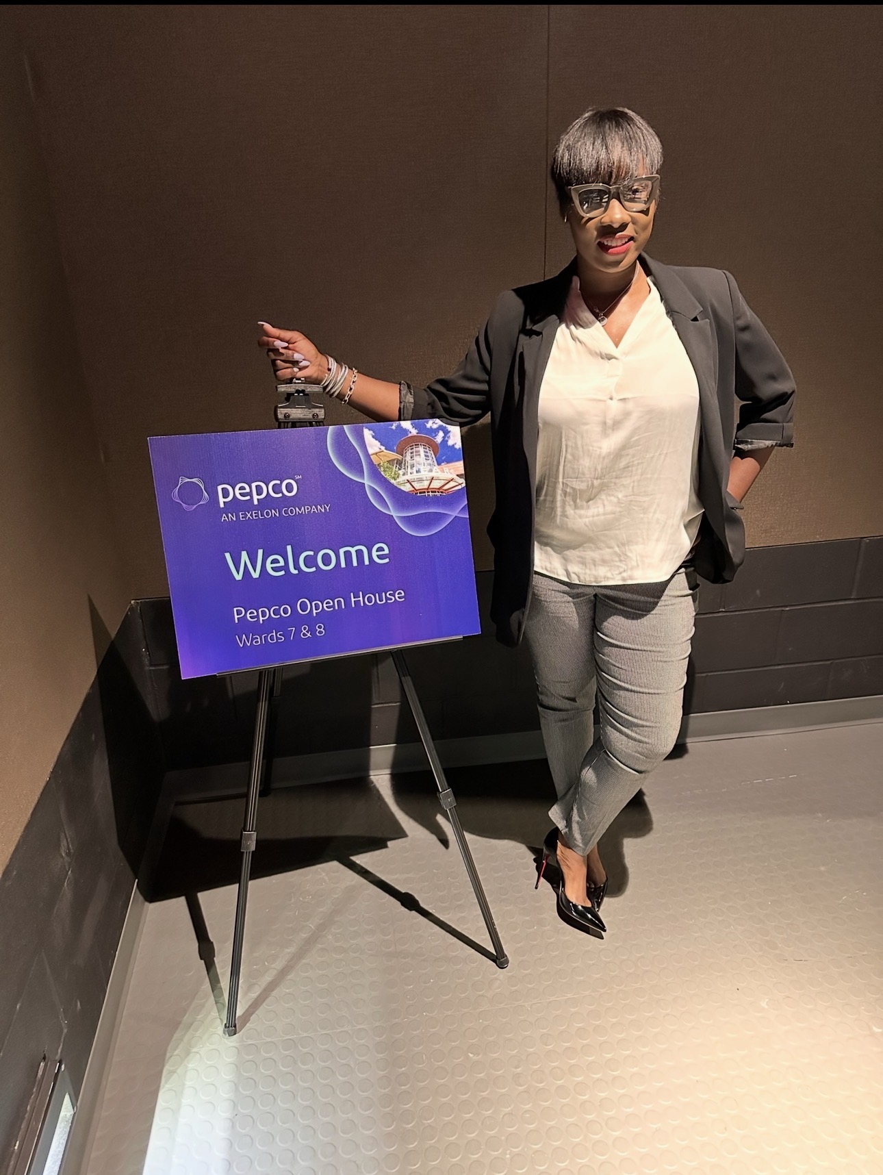 Woman in business attire standing next to a welcome sign at Pepco Open House event.