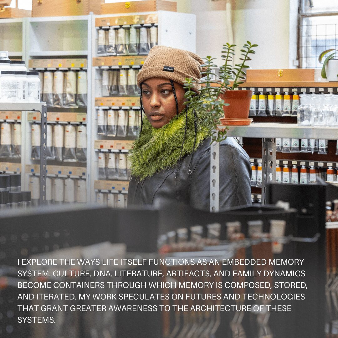 Woman wearing a beige beanie and black jacket in a store with shelves of jars and plants behind her.