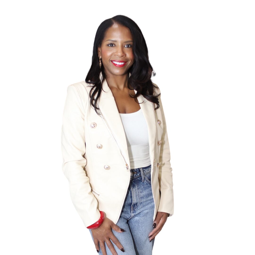 Woman with long dark hair, wearing a white blazer, white top, and jeans, smiling against a white background.