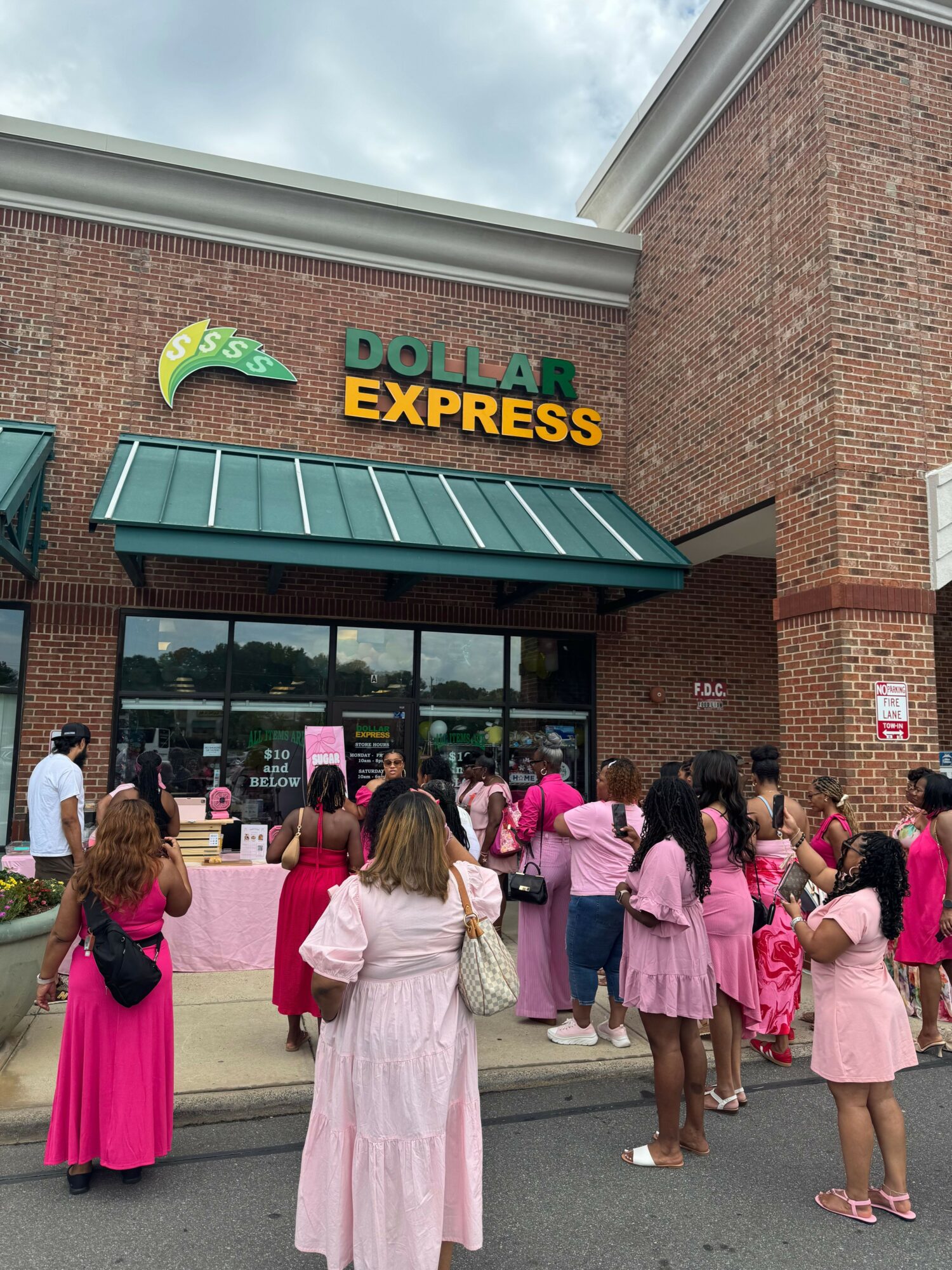 Group of women and girls in pink dresses standing outside a building with a sign that reads 'Oklahoma City Express'.
