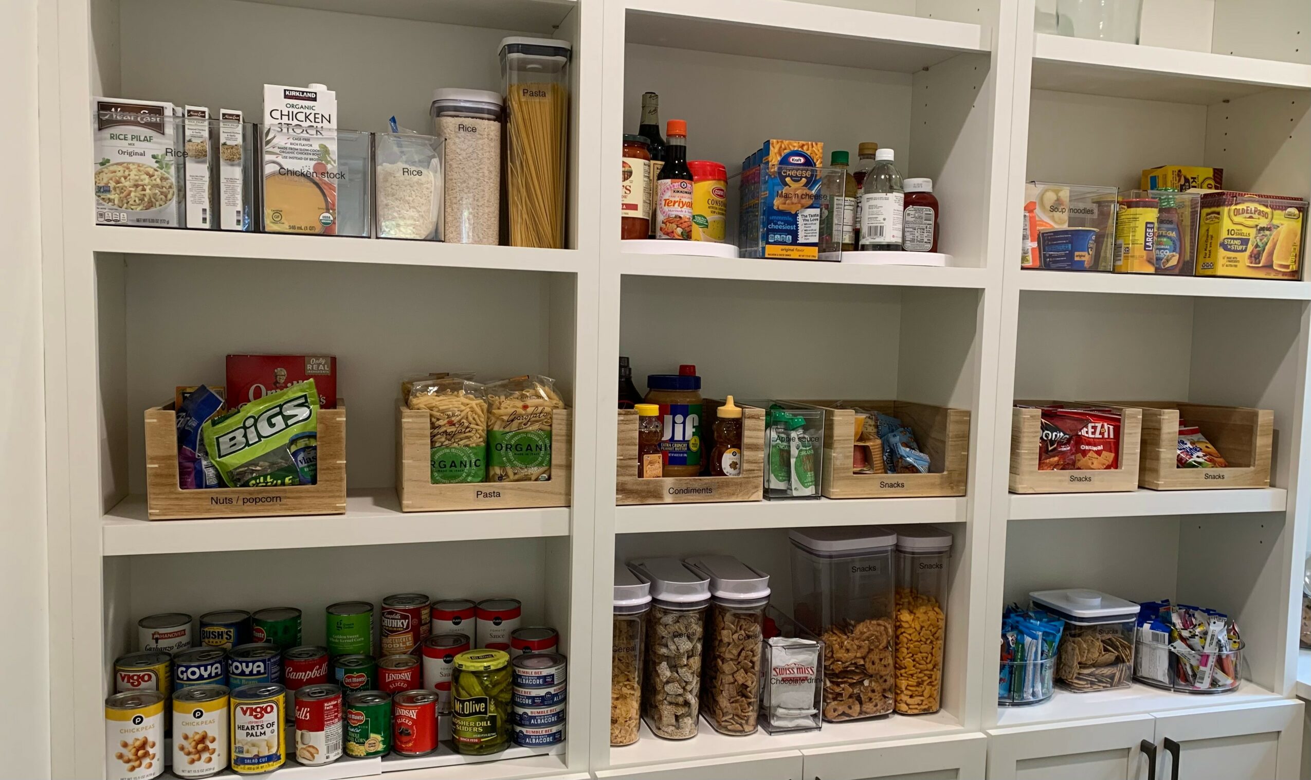 Shelves filled with various food items, snacks, canned goods, and jars organized in baskets and containers.
