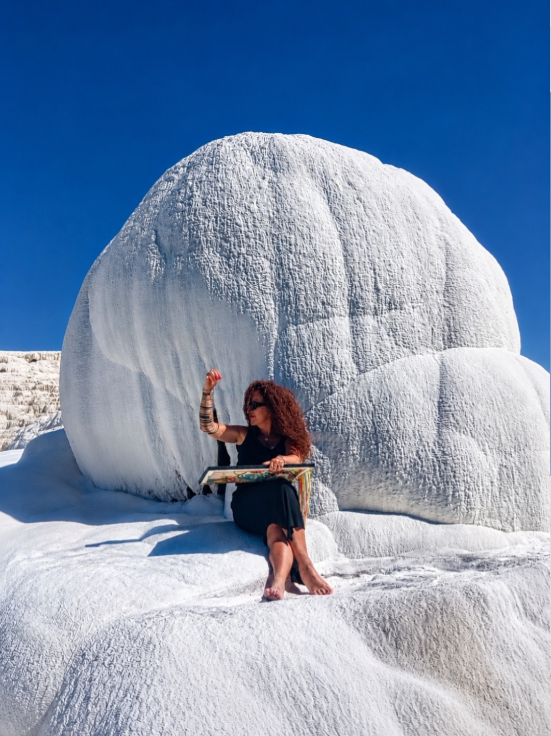Person sitting on snow with a large snow sculpture behind them, clear blue sky, snow-covered landscape.