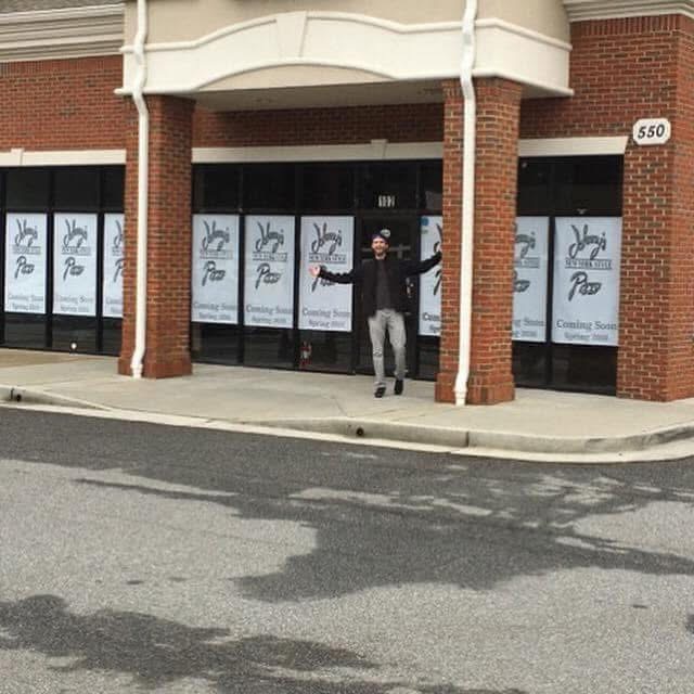 Person standing outside a storefront with large windows, holding a sign, in front of a brick building.