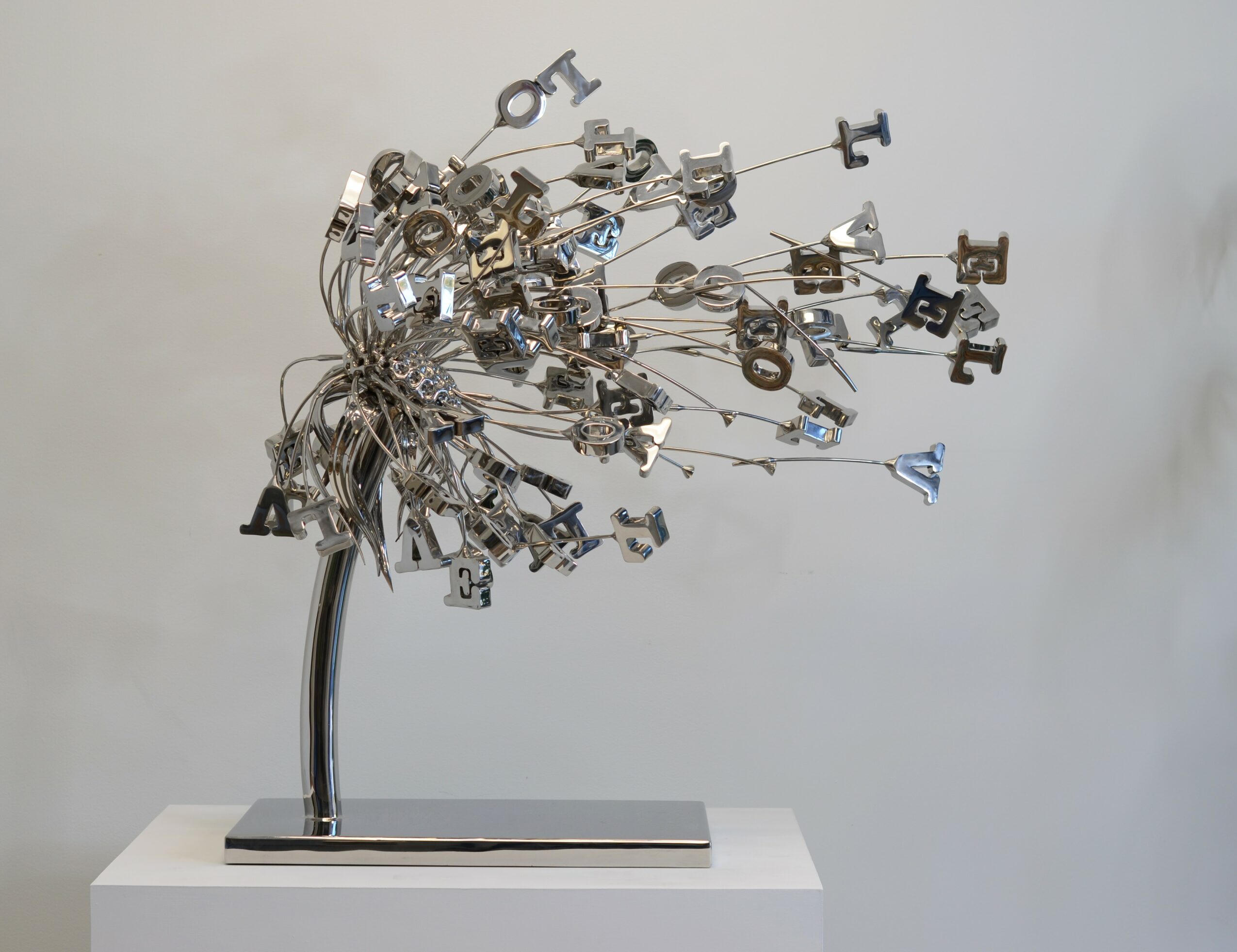Sculpture of a tree made from metal keys and objects on a white base, with a plain light background.
