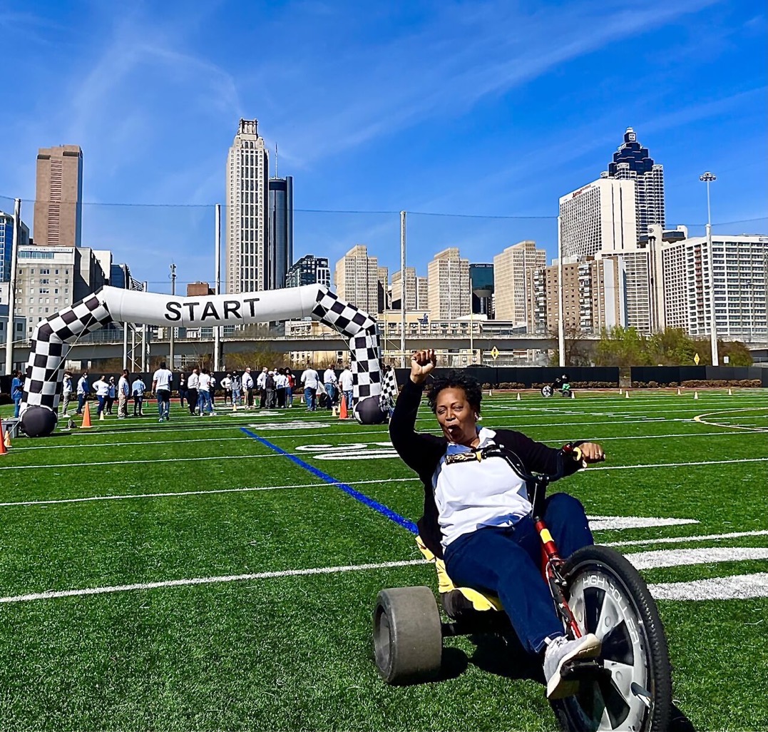 Person on a tricycle in front of a start line on a sports field with city skyline in background.