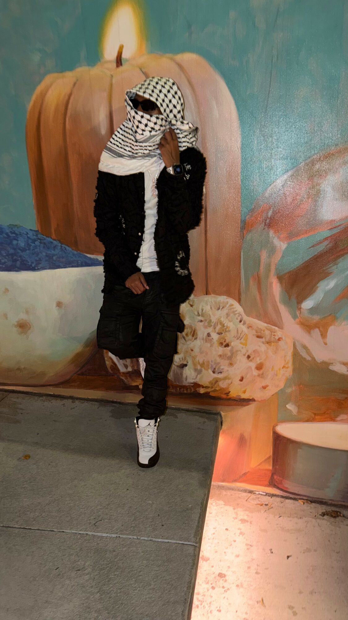 Person standing in front of a large pumpkin and decorative objects, wearing a striped hoodie and black pants.