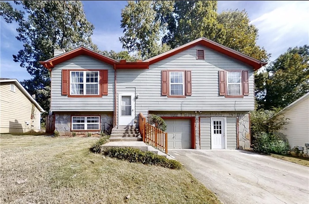 Two-story house with white siding, red shutters, and a front staircase, surrounded by trees and neighboring houses.