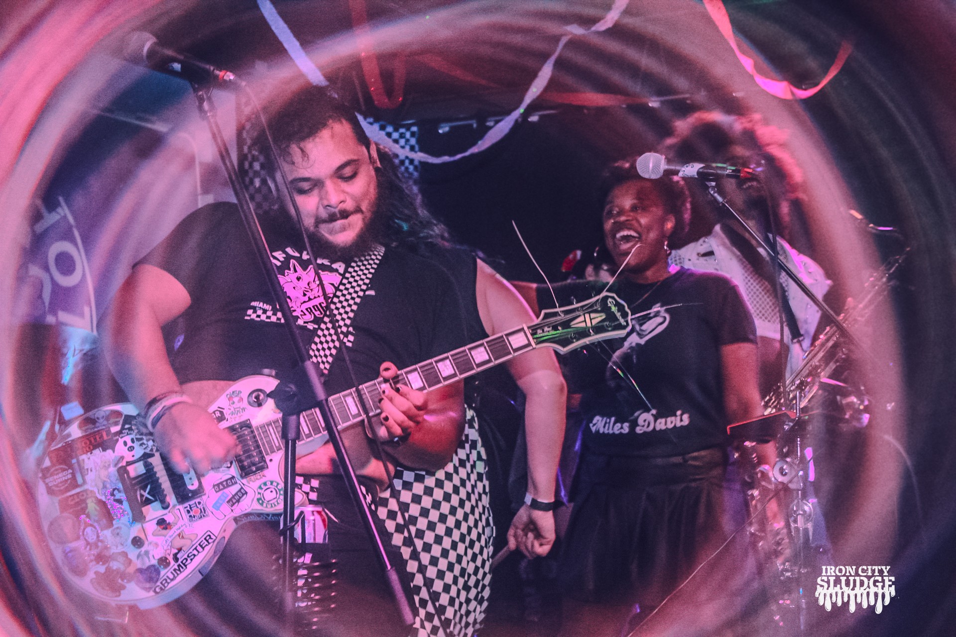 Two musicians perform on stage, one playing guitar and the other singing, with colorful stage lighting effects.