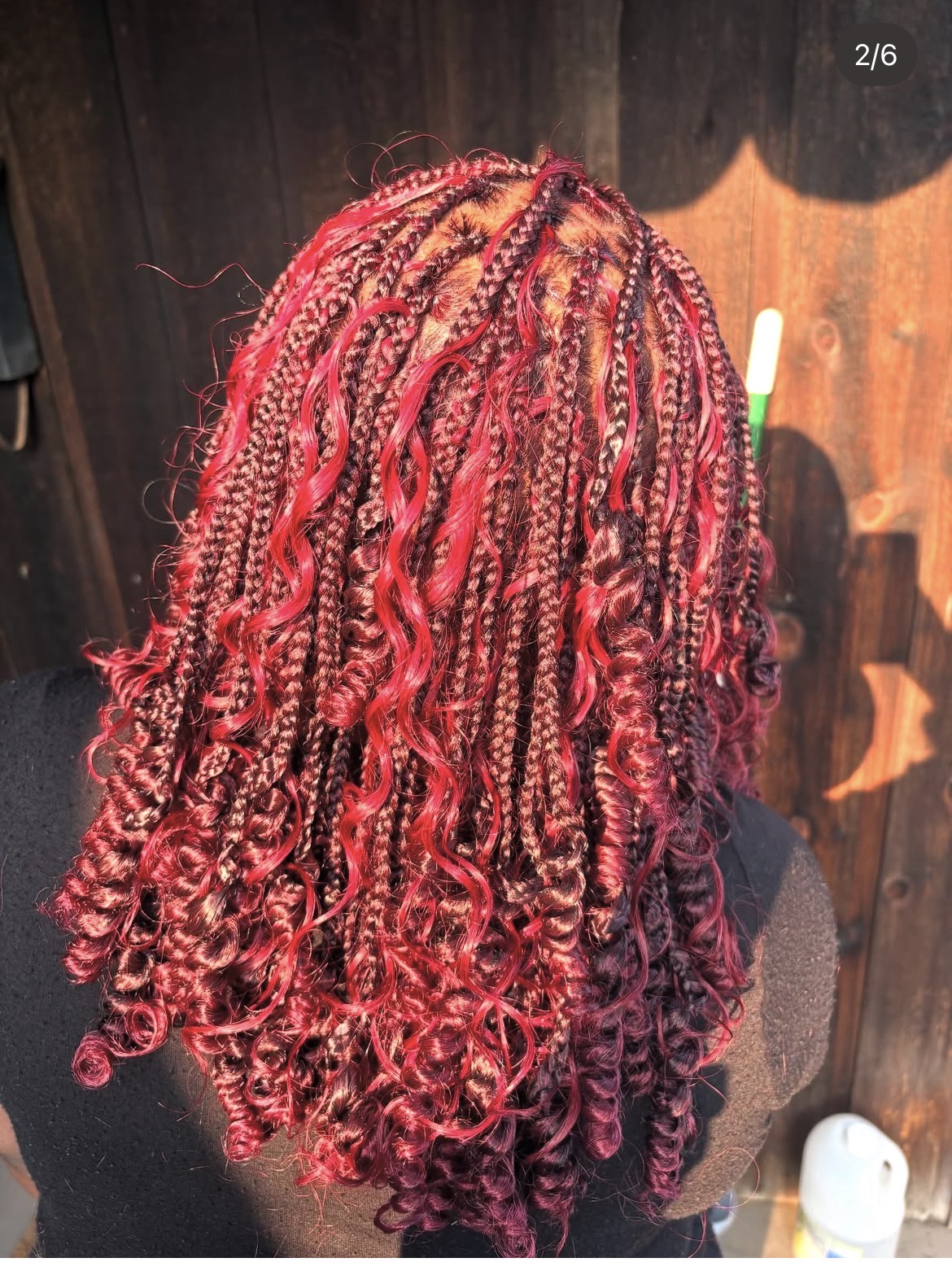 Back of a person with long, curly, red and black braided hair outdoors, wooden fence background.