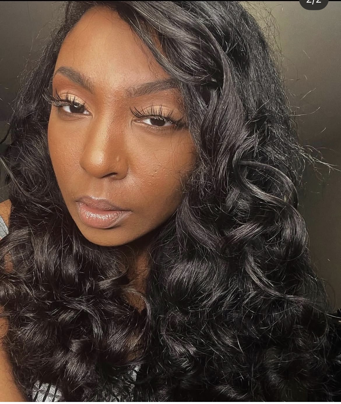 Close-up of a woman with long, curly black hair and makeup, looking at the camera.
