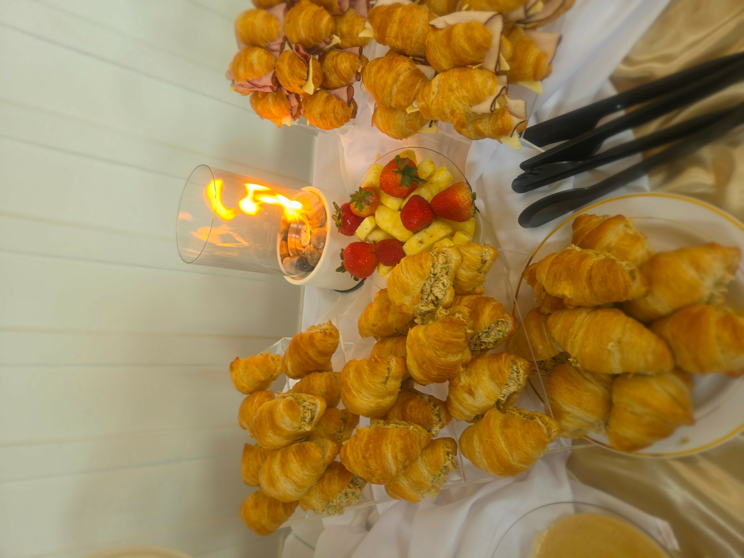 Table with small pastries, strawberries, and a lit candle, viewed from the side, with a white background.