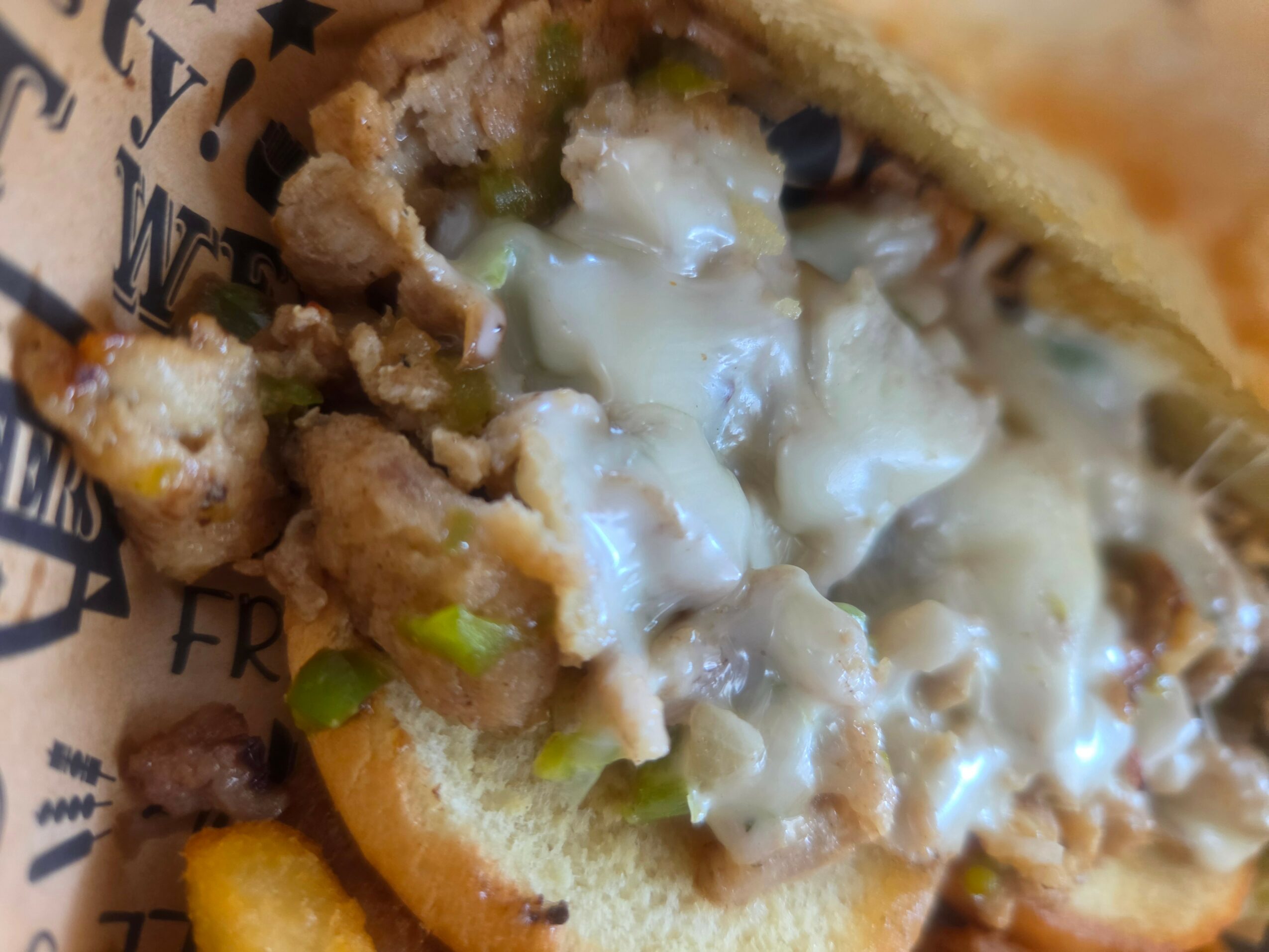 Close-up of a sandwich with melted cheese, cooked meat, and green onions inside a bun.