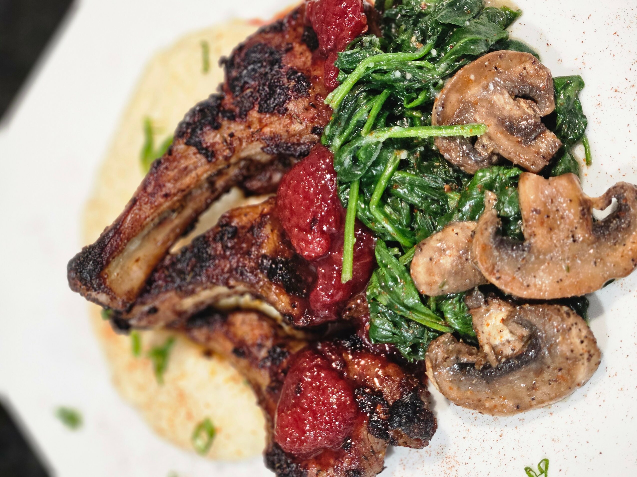 Roasted meat with tomato sauce, sautéed spinach with mushrooms, served on a white plate.
