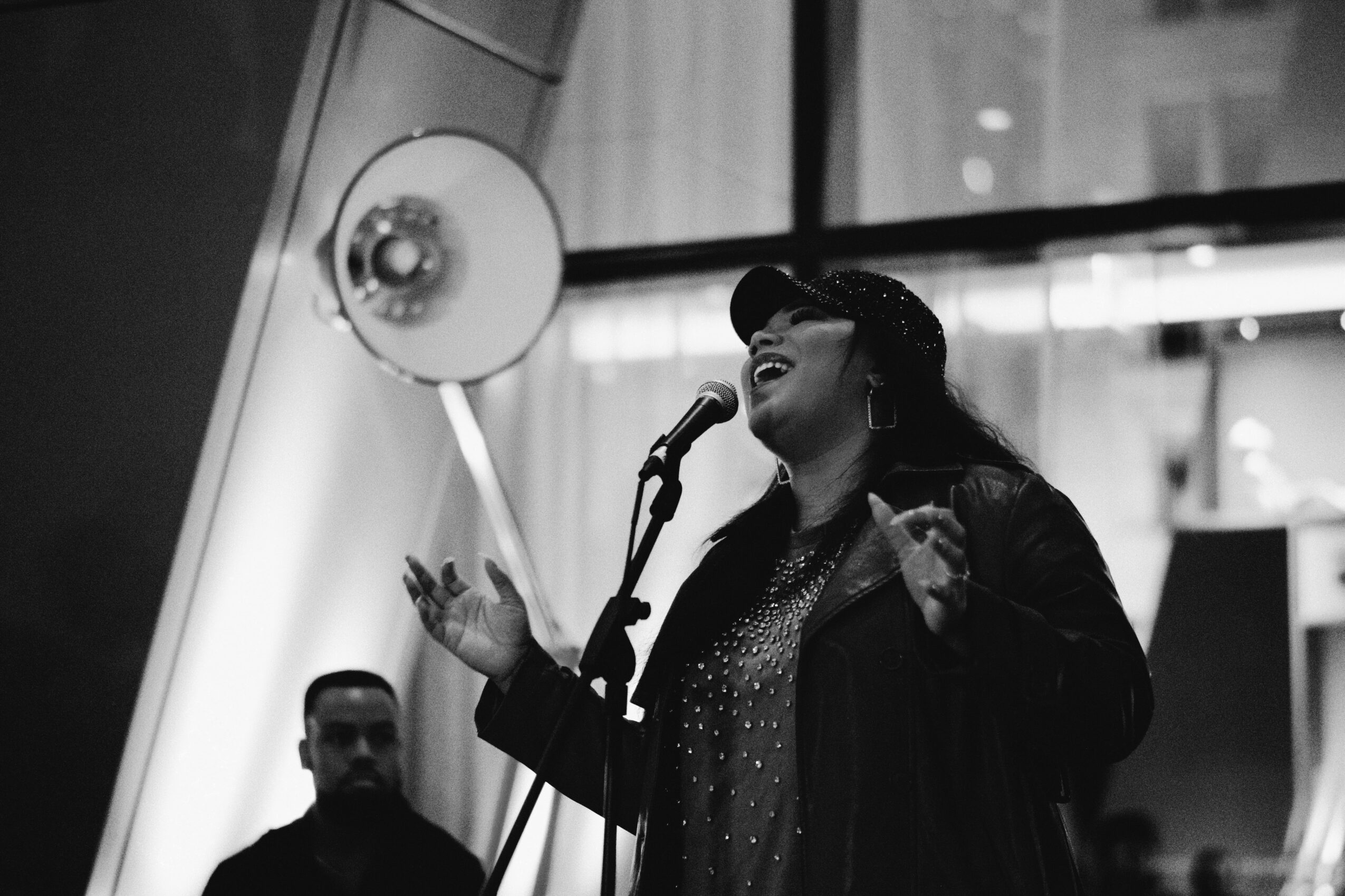 A woman singing into a microphone with a person in the background, in black and white.