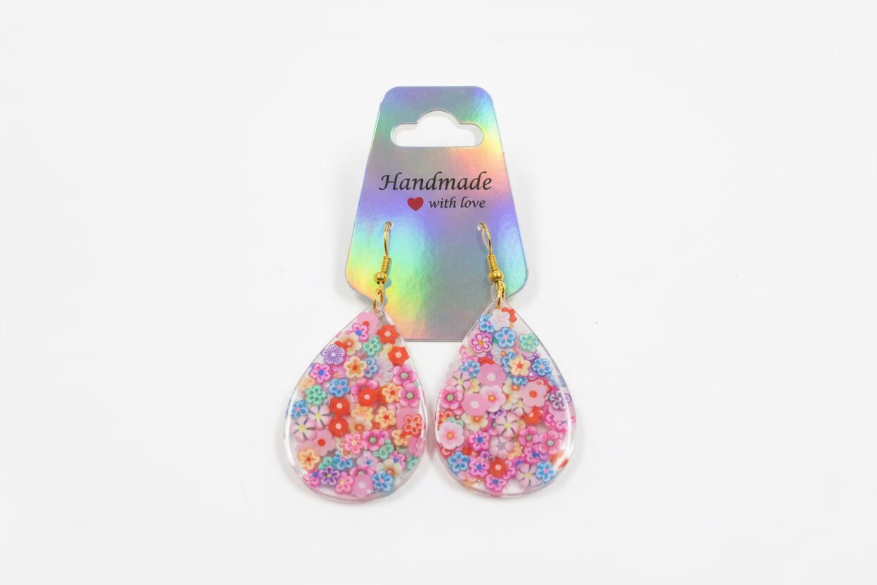 Colorful teardrop-shaped earrings with floral patterns on a white background, attached to a rainbow-colored card that says 'Handmade with Love'.