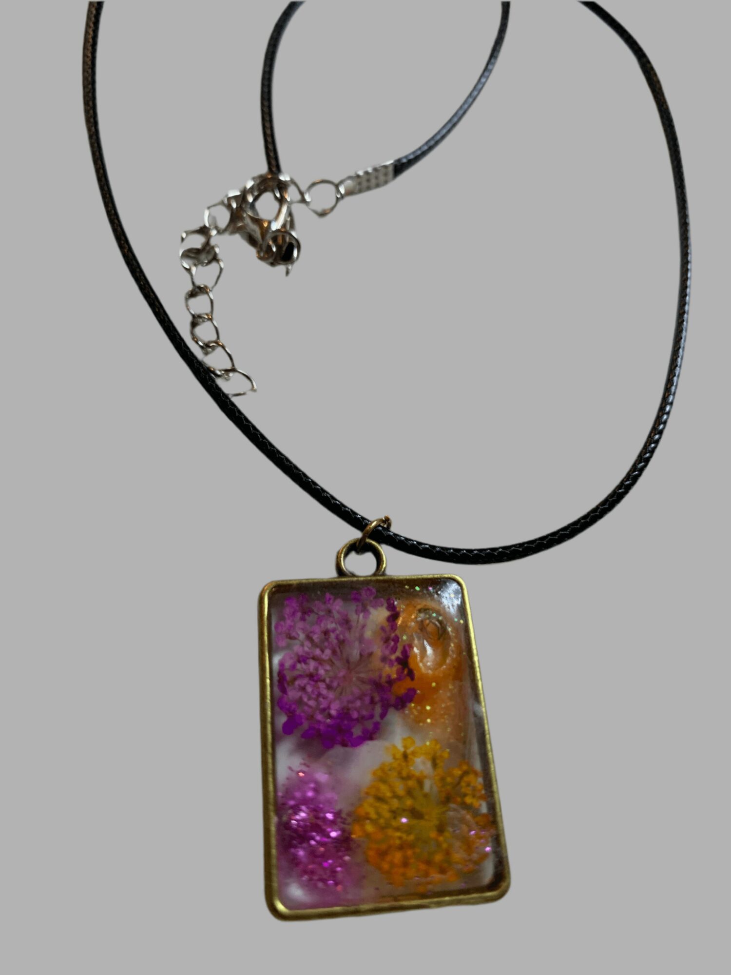 Pendant necklace with a rectangular, colorful, floral design, on a black cord with a silver clasp.