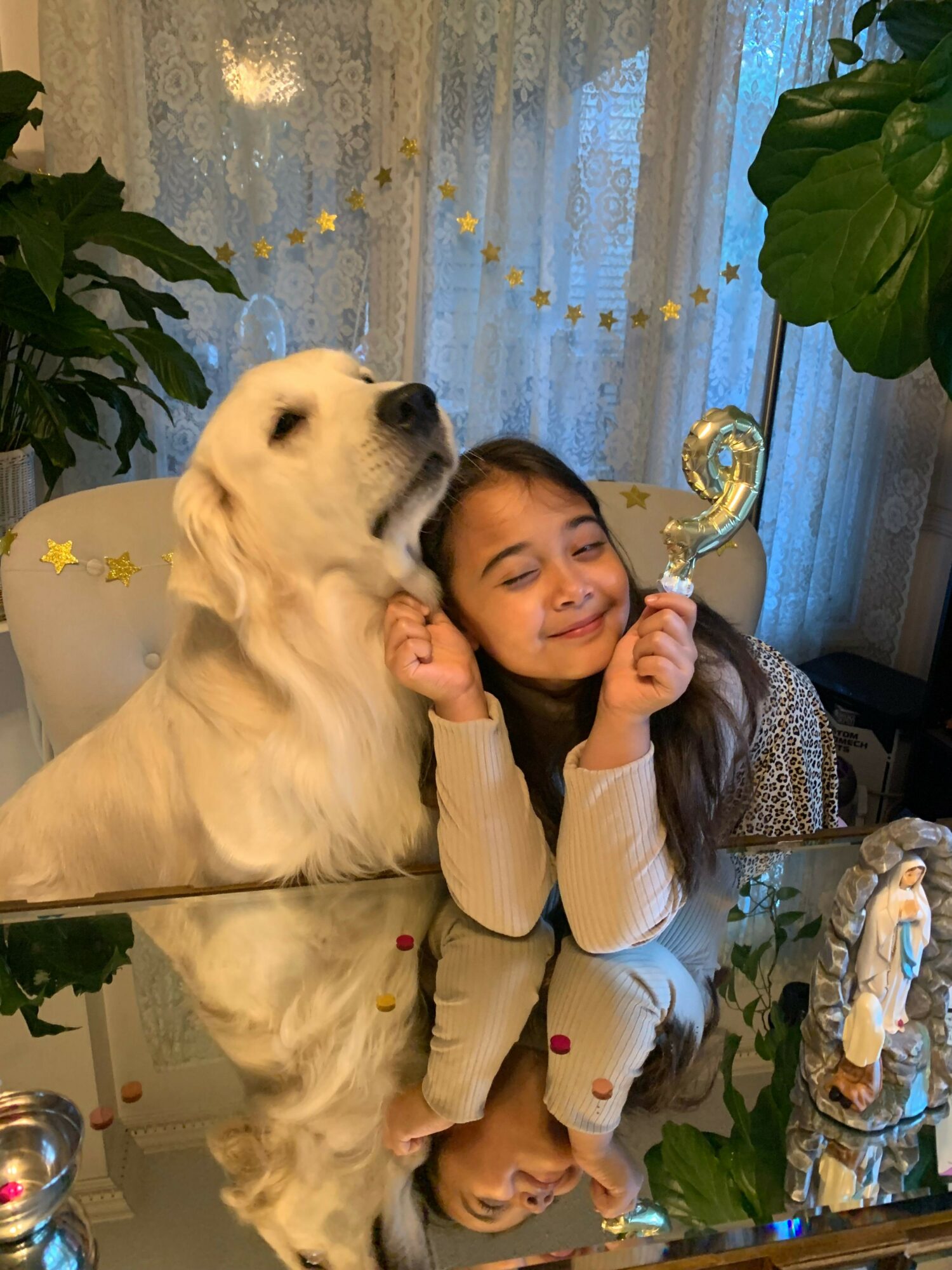 Girl lying on floor with a large white dog, surrounded by plants and decorative stars, indoors.