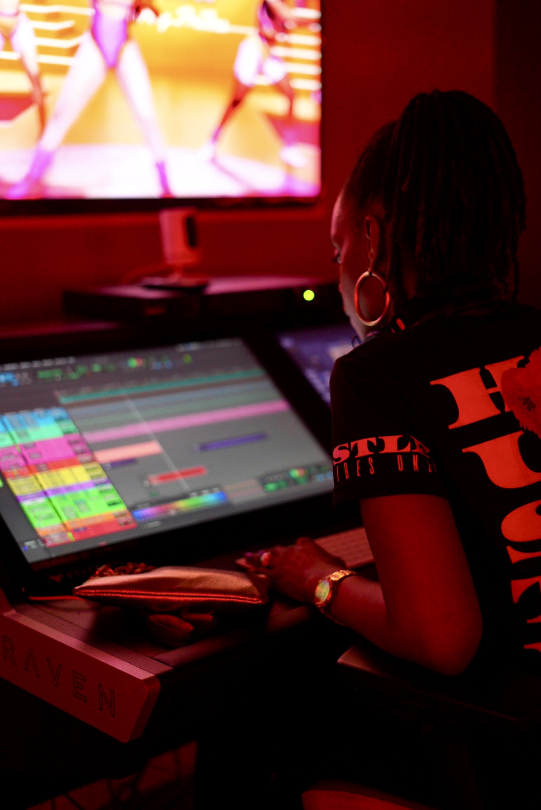 Person working on music production with a computer and large screen in a dimly lit room.