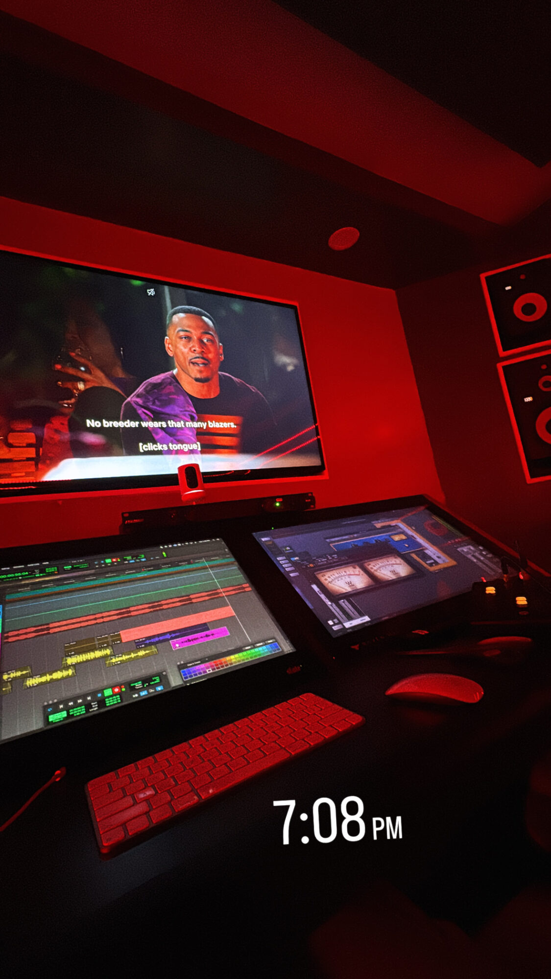 Recording studio with a large screen showing a person speaking, and a mixing console with a tablet, in red lighting.