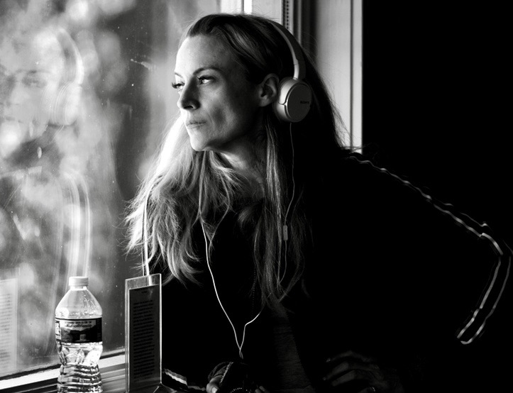 Woman with headphones looking out window, water bottle and speaker on table, black and white photo.