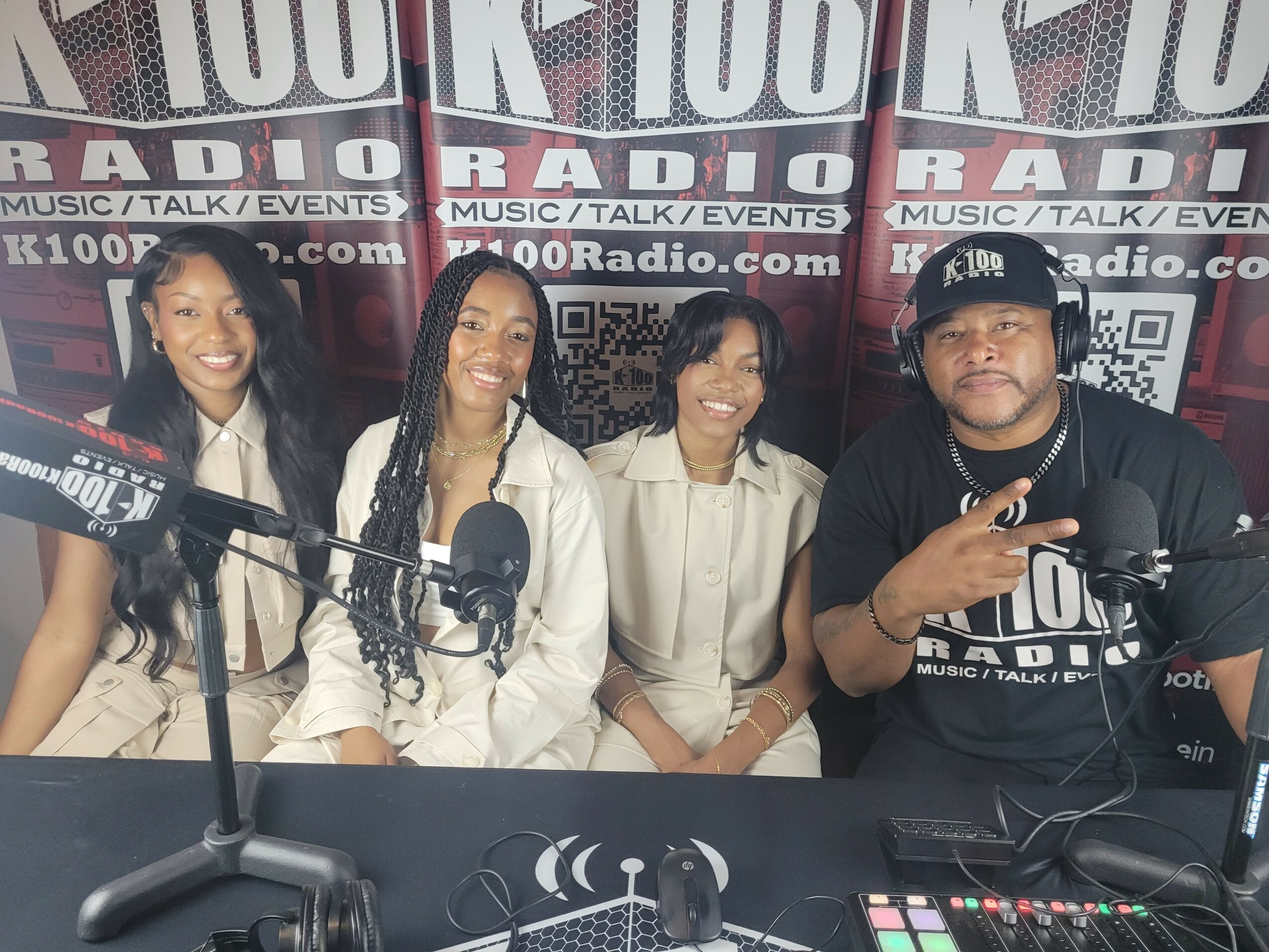 Four people sit at a radio station table with microphones, smiling, in front of a backdrop with radio station branding.