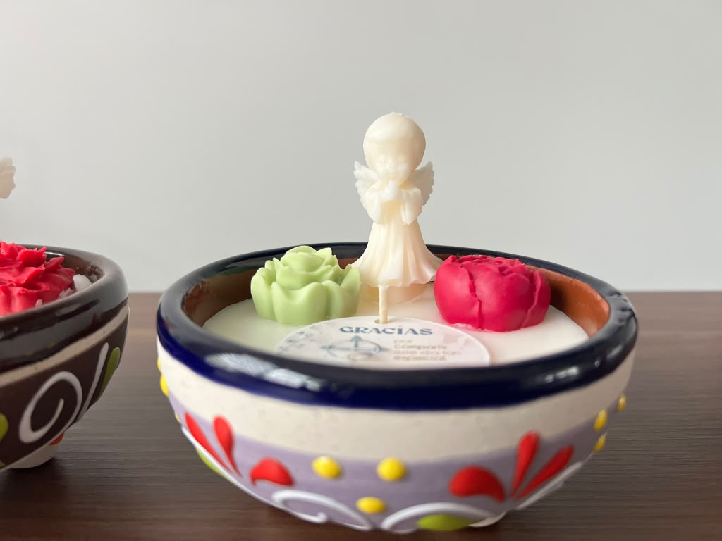 Decorative bowl with a small angel figurine, a green flower, and a red flower, on a wooden surface.