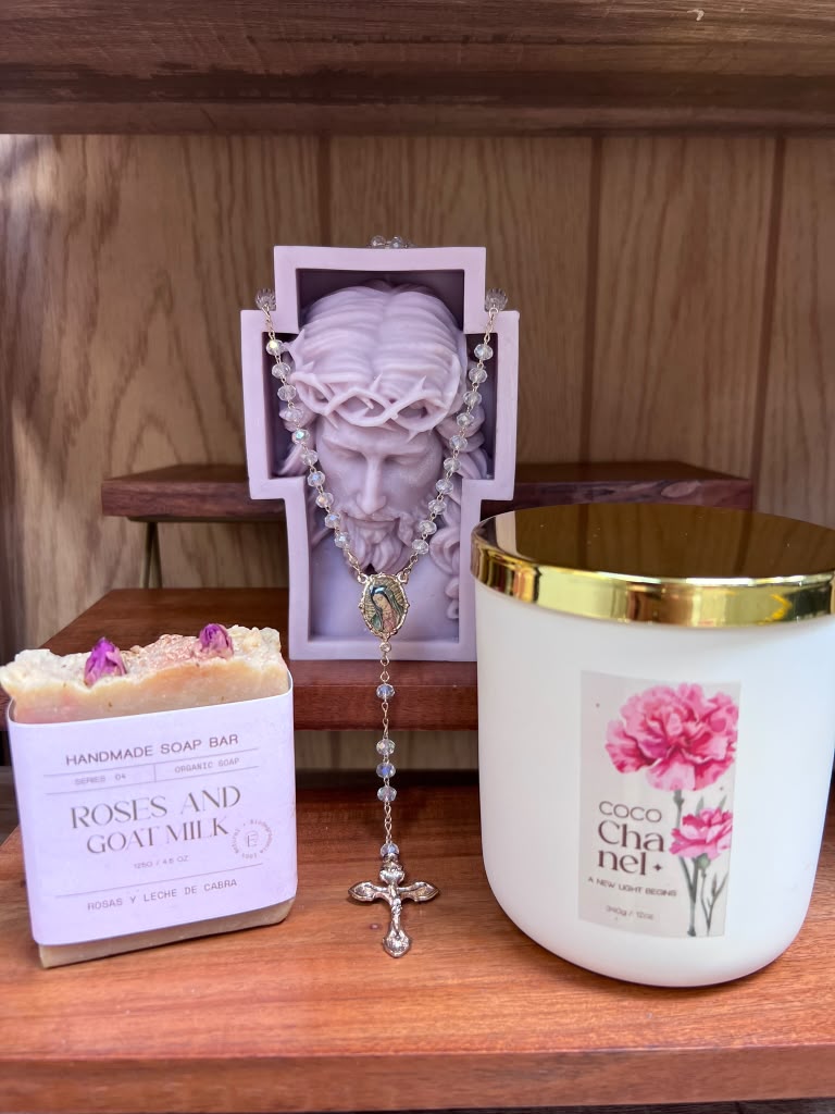 Decorative jewelry display with a necklace, a candle with pink flowers, and a soap bar on a wooden shelf.