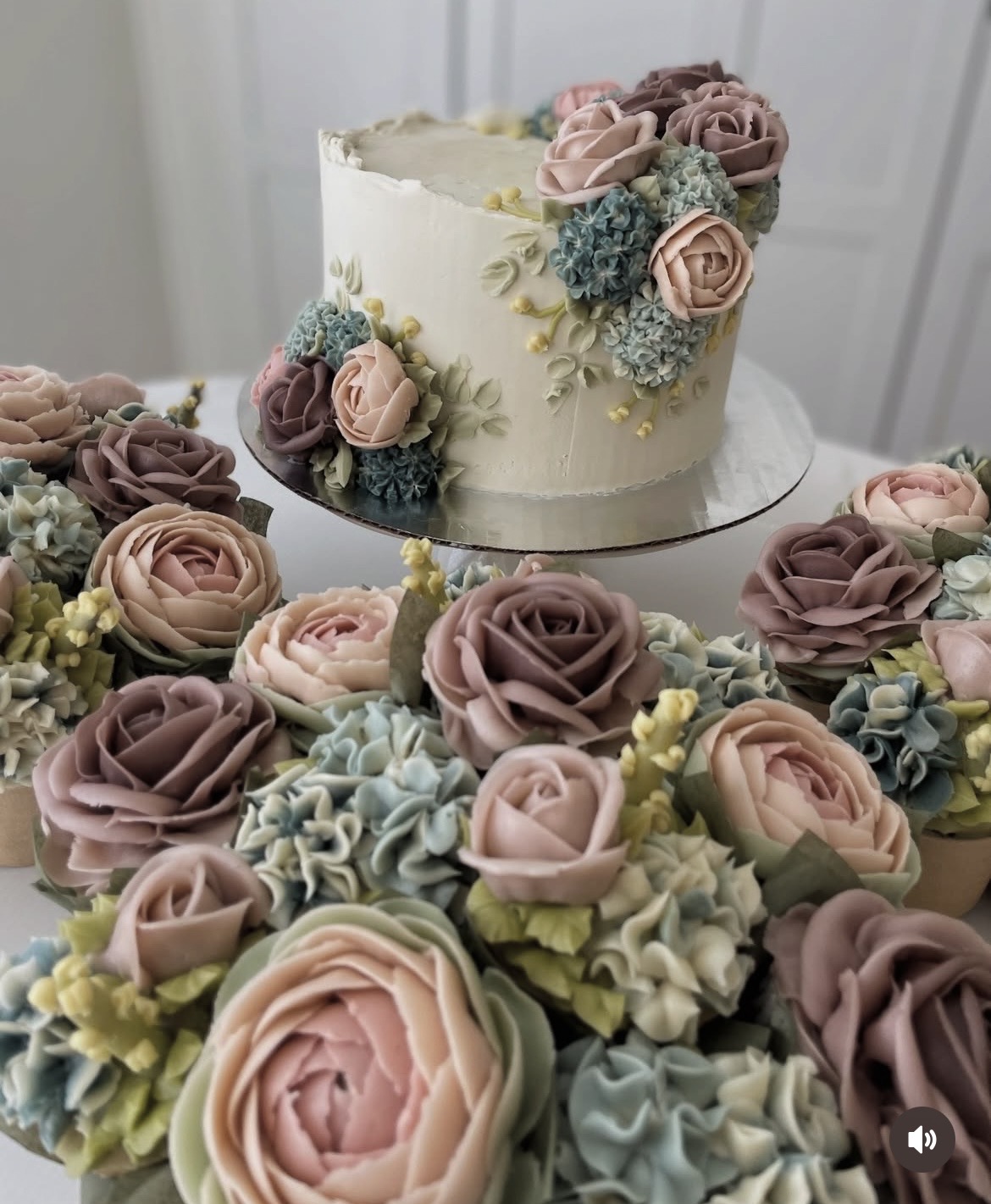 A decorated cake with pink, purple, and blue flowers, surrounded by matching floral decorations, on a table.