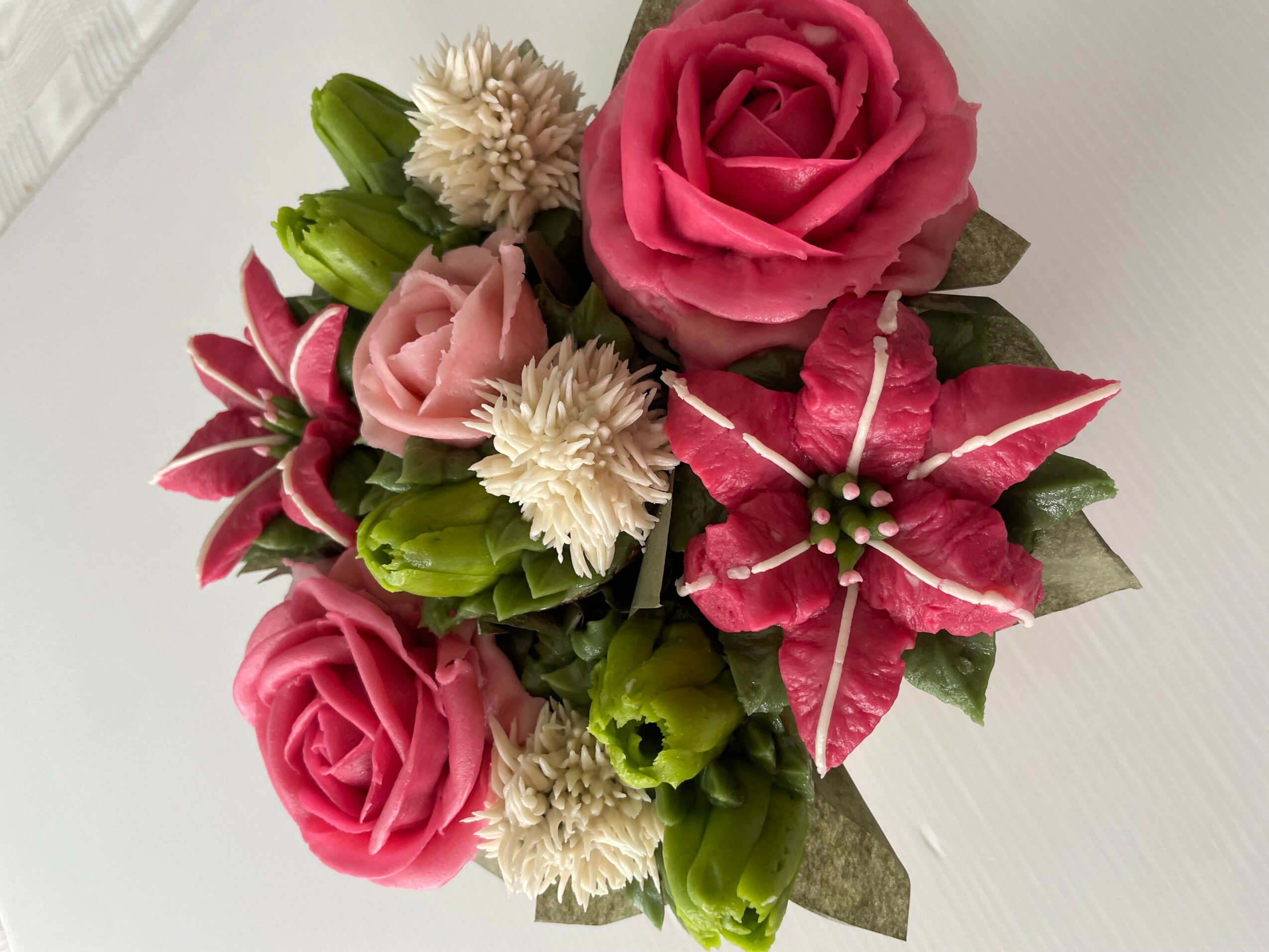 A bouquet of pink roses, white flowers, and a pink poinsettia with green leaves, arranged in a circular pattern.