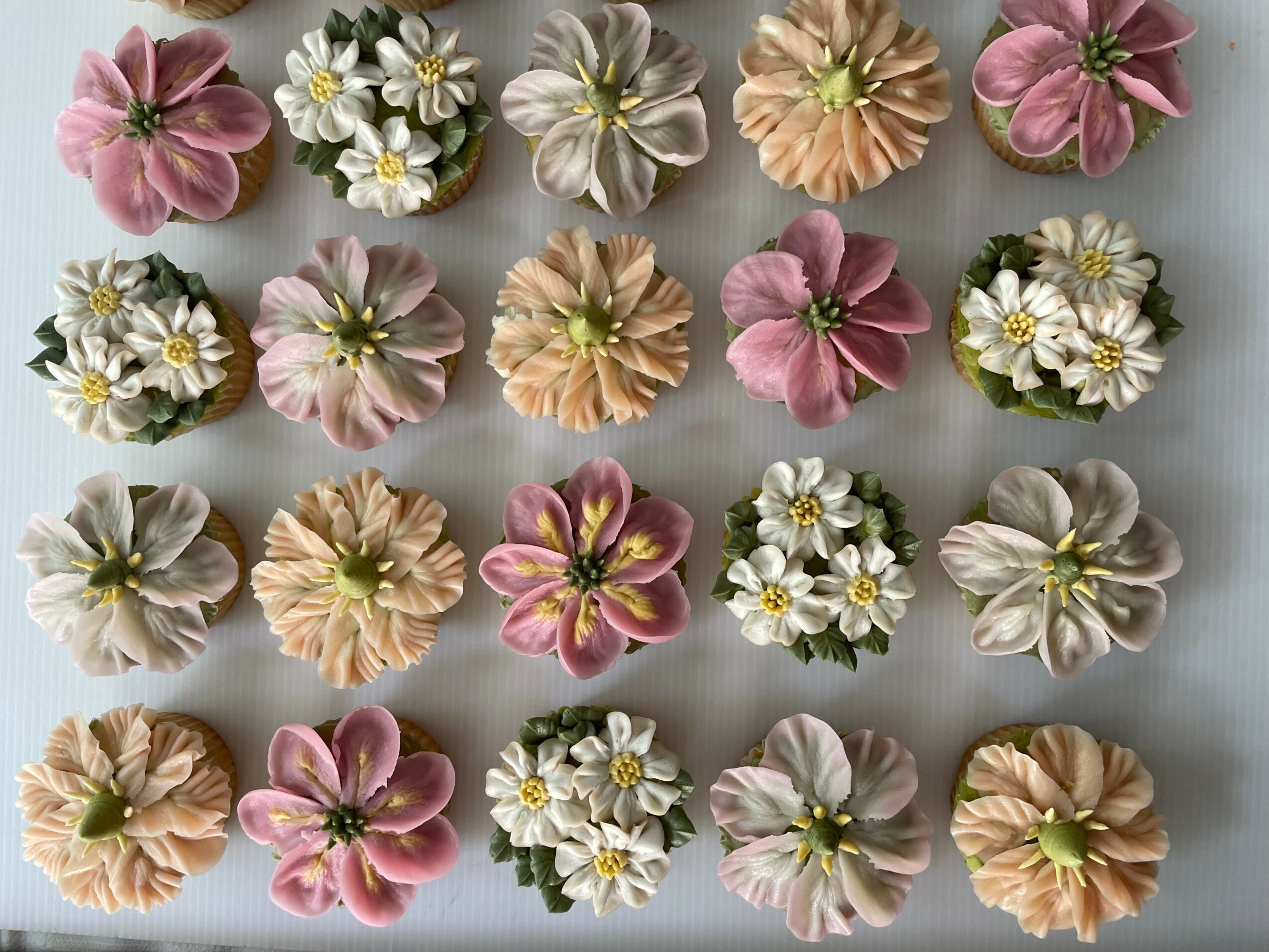 Arrangement of pink, peach, white, and yellow flowers with green centers, evenly spaced on a light background.
