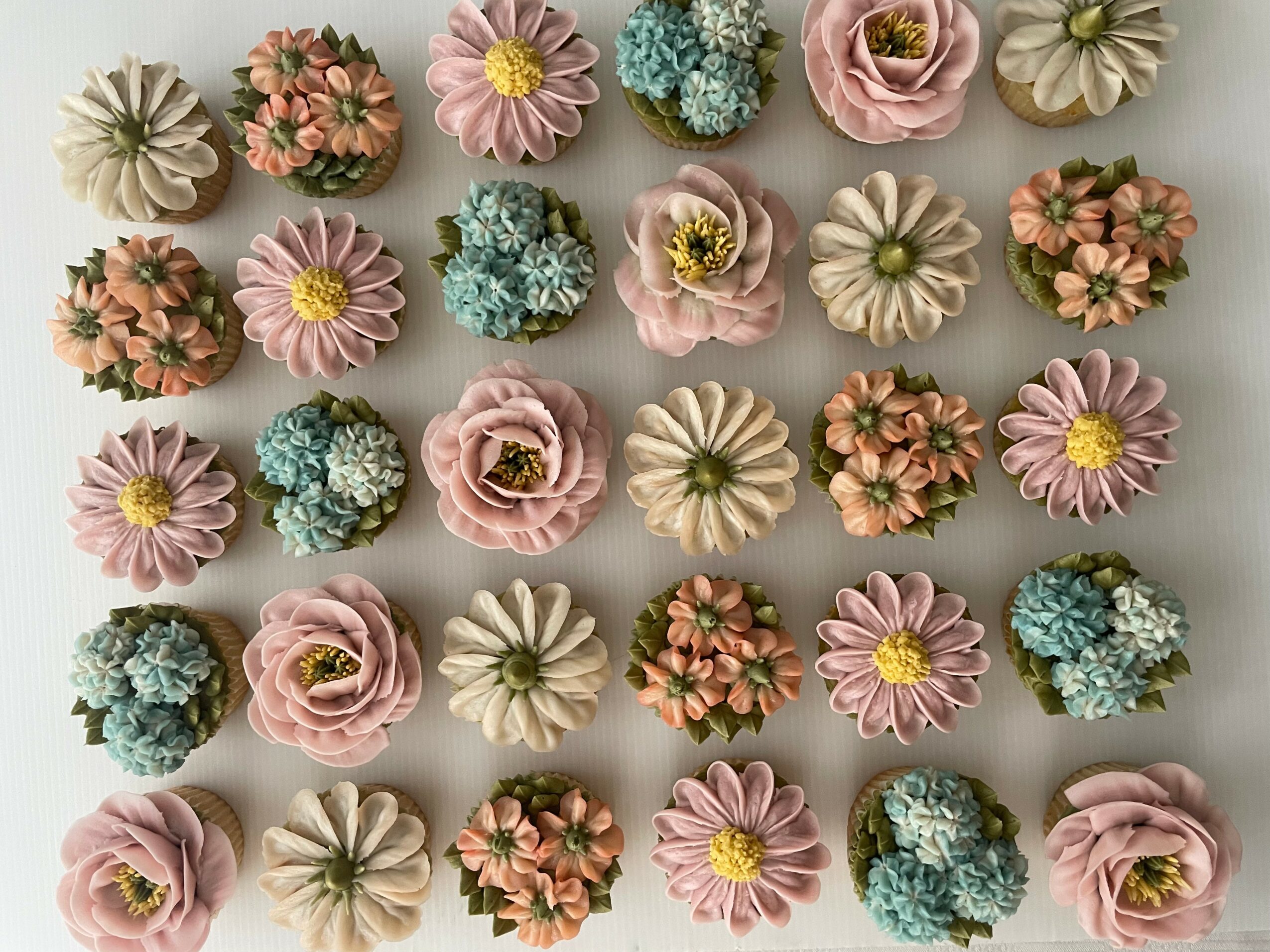 Arrangement of colorful flowers including pink, white, blue, and peach blooms on a neutral background.