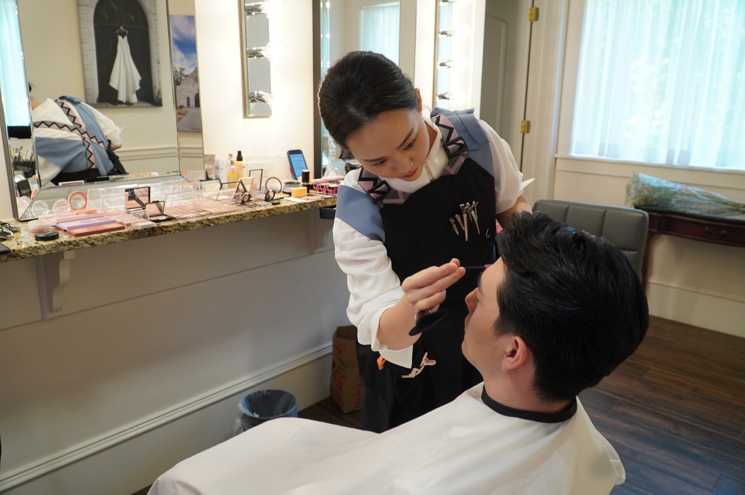Person getting makeup or skincare applied by a makeup artist in a room with a mirror and vanity table.