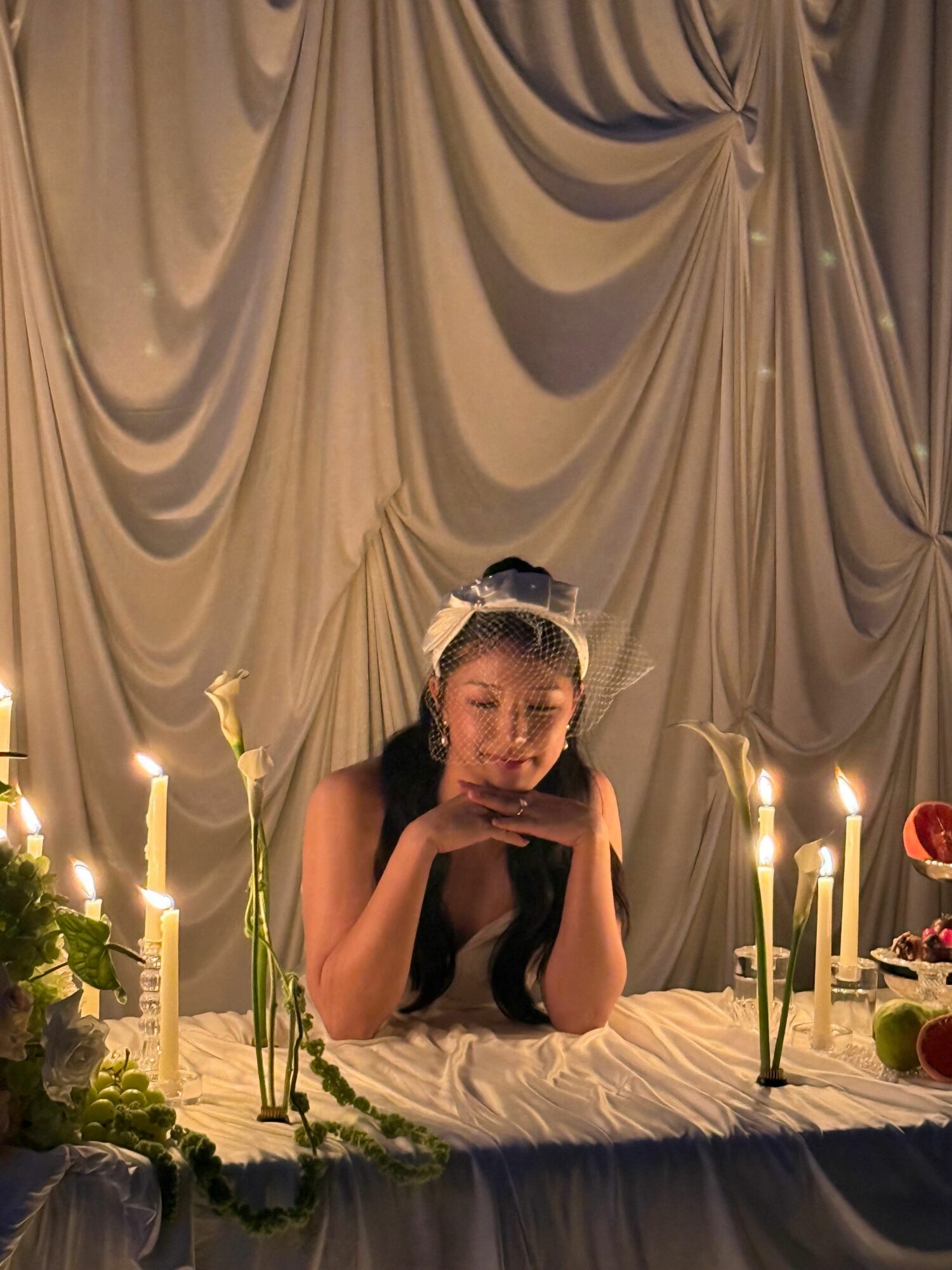 Young woman with long dark hair and a headband, resting her chin on her hand at a decorated table with candles and flowers.