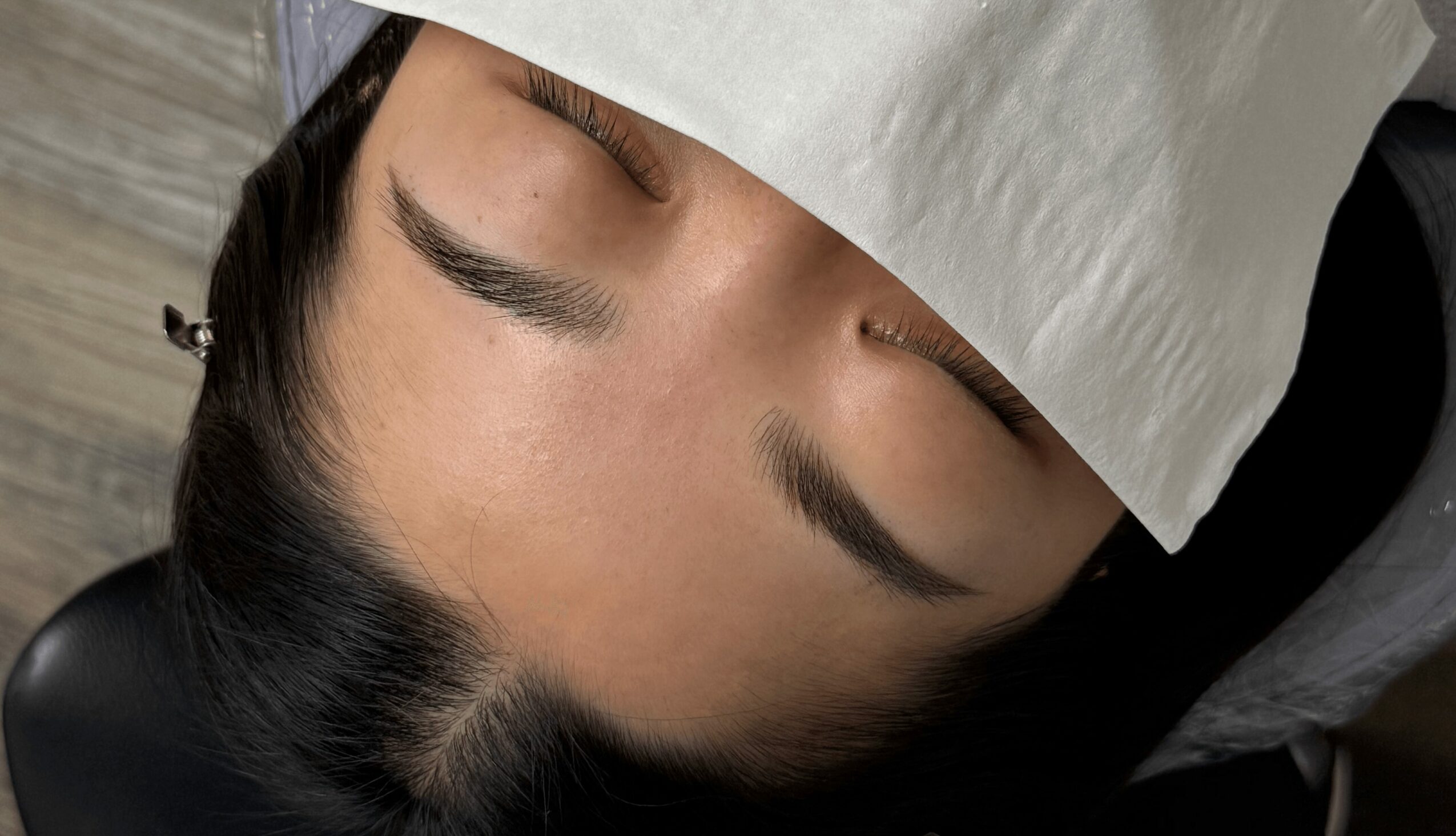 Person with closed eyes, lying down, covered with a white cloth, with dark hair and makeup visible.