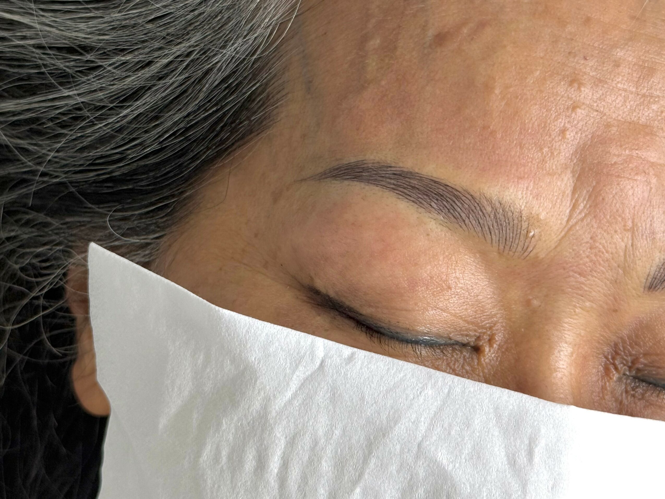 Close-up of a person's face with eyes closed, showing eyebrows and part of a white cloth covering the cheek.