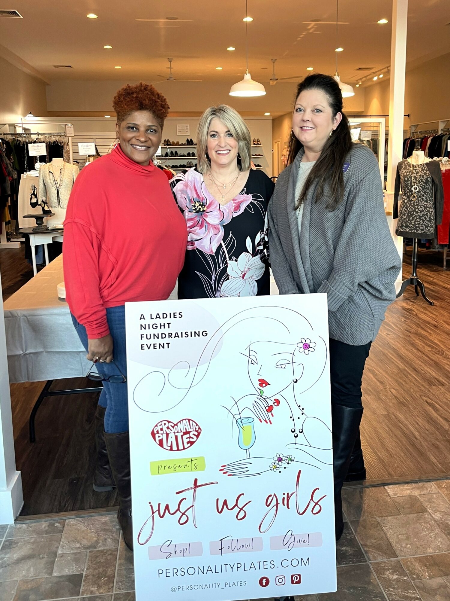 Three women standing indoors behind a sign for a ladies' night event, smiling at the camera.