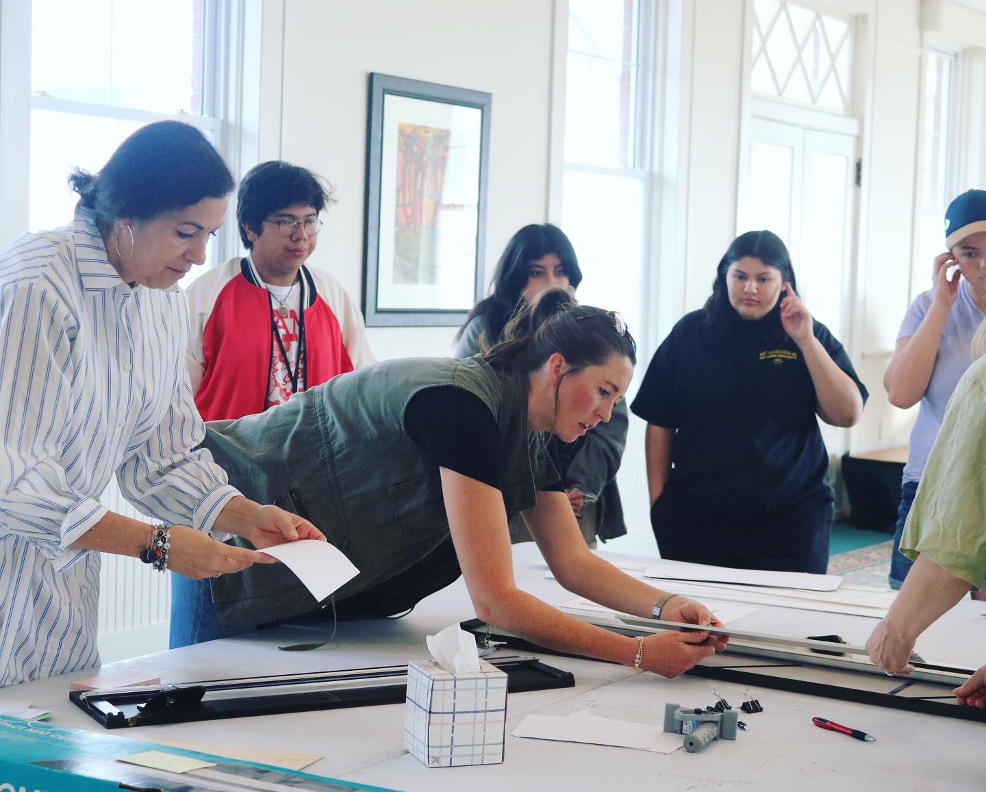 Group of people gathered around a table with tools and a cube, engaging in a hands-on activity in a bright room.