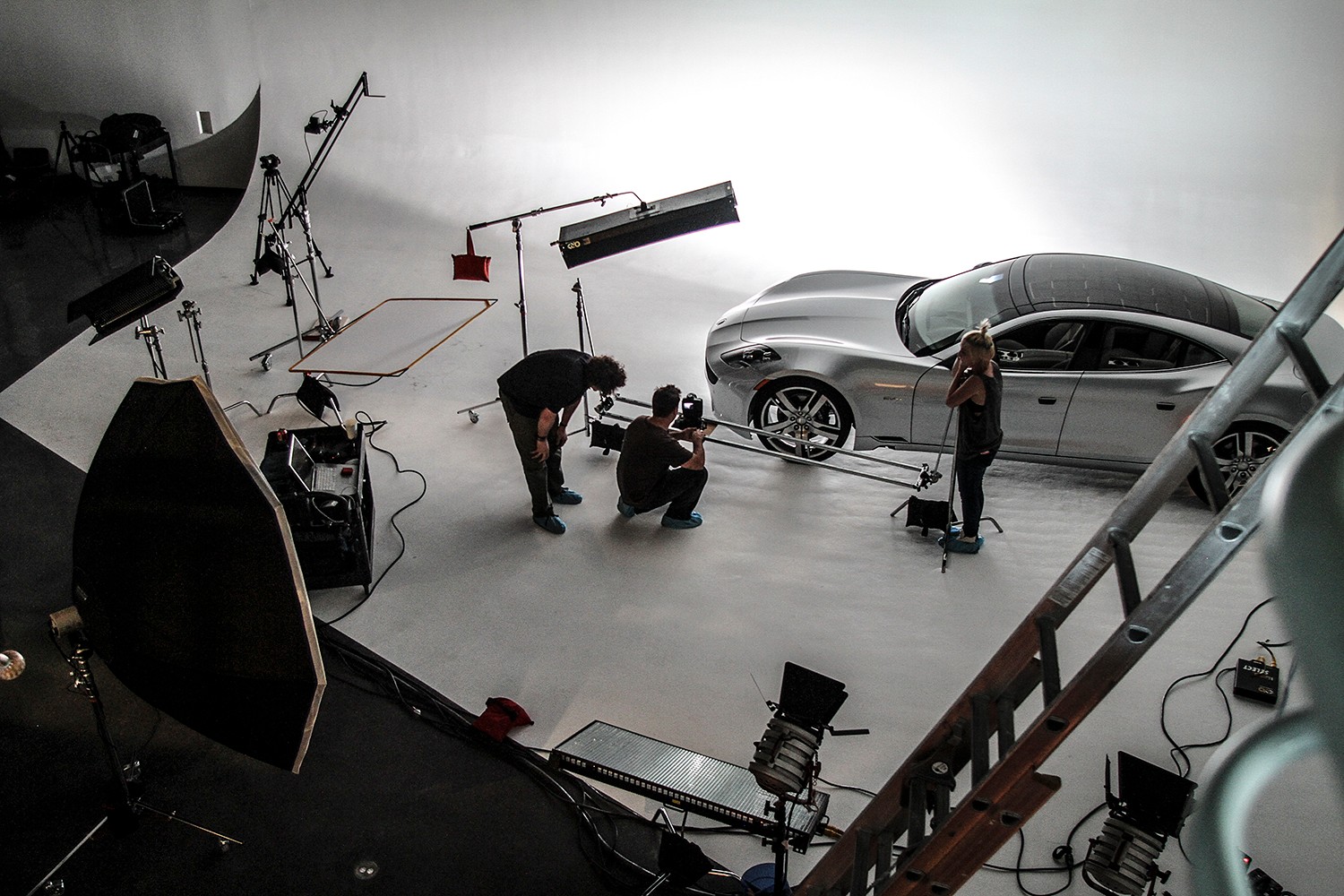 Studio setup with a silver car, crew members, and photography equipment in a large, well-lit space.