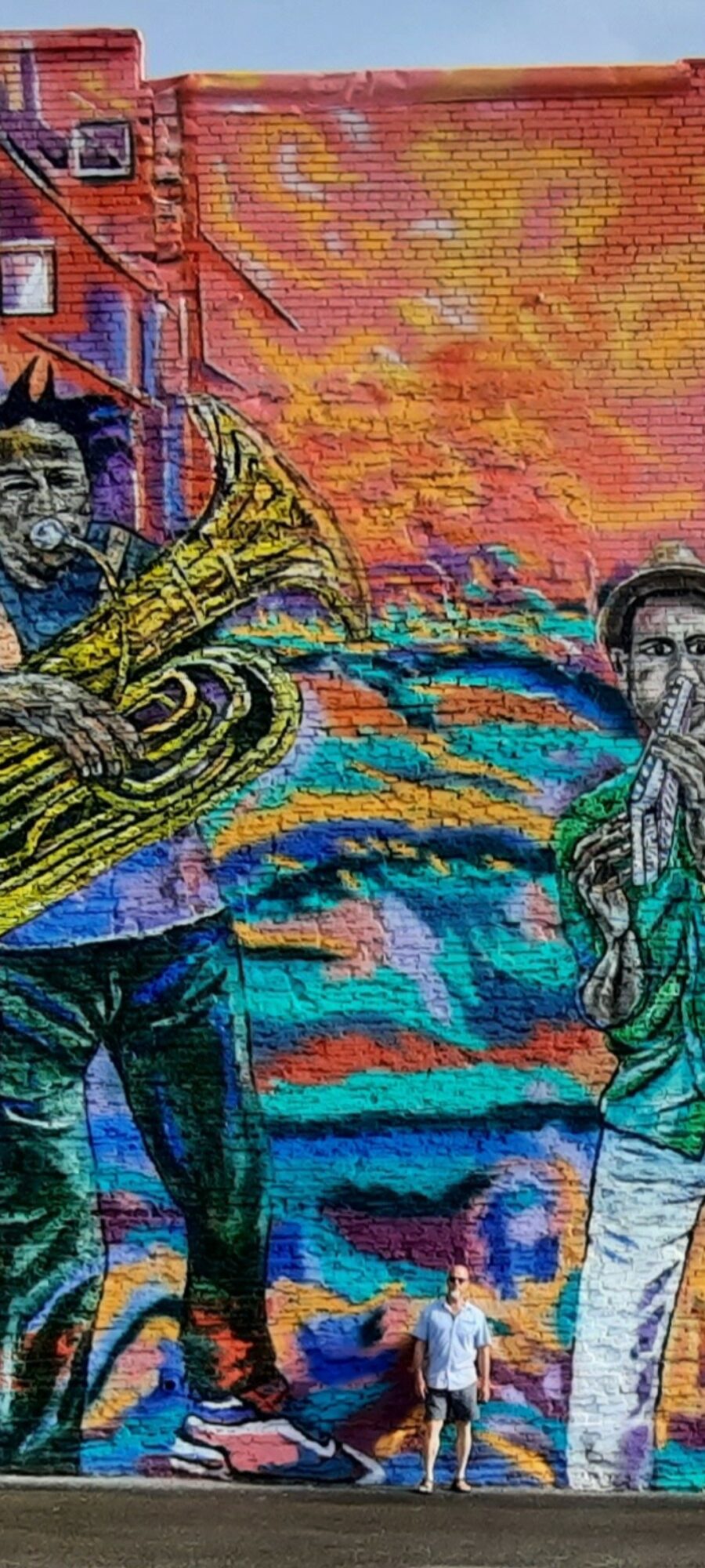 Colorful mural with two people, one playing a guitar, against a vibrant sunset background.