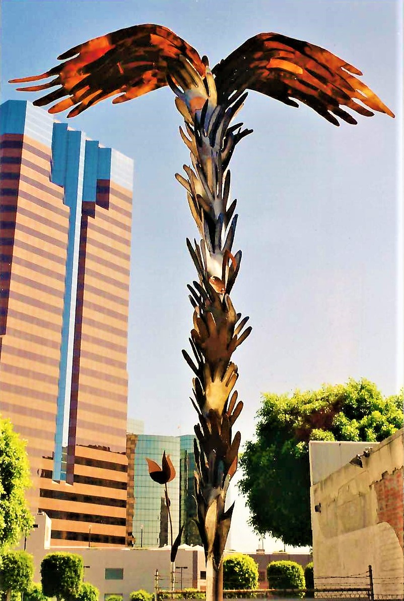 Tall sculpture of a bird with outstretched wings made of metal feathers, set against a cityscape with buildings and trees.