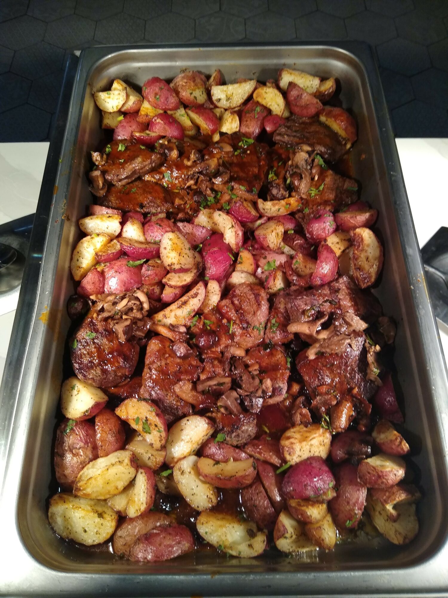 Baked dish with chunks of meat and roasted potatoes in a metal tray.