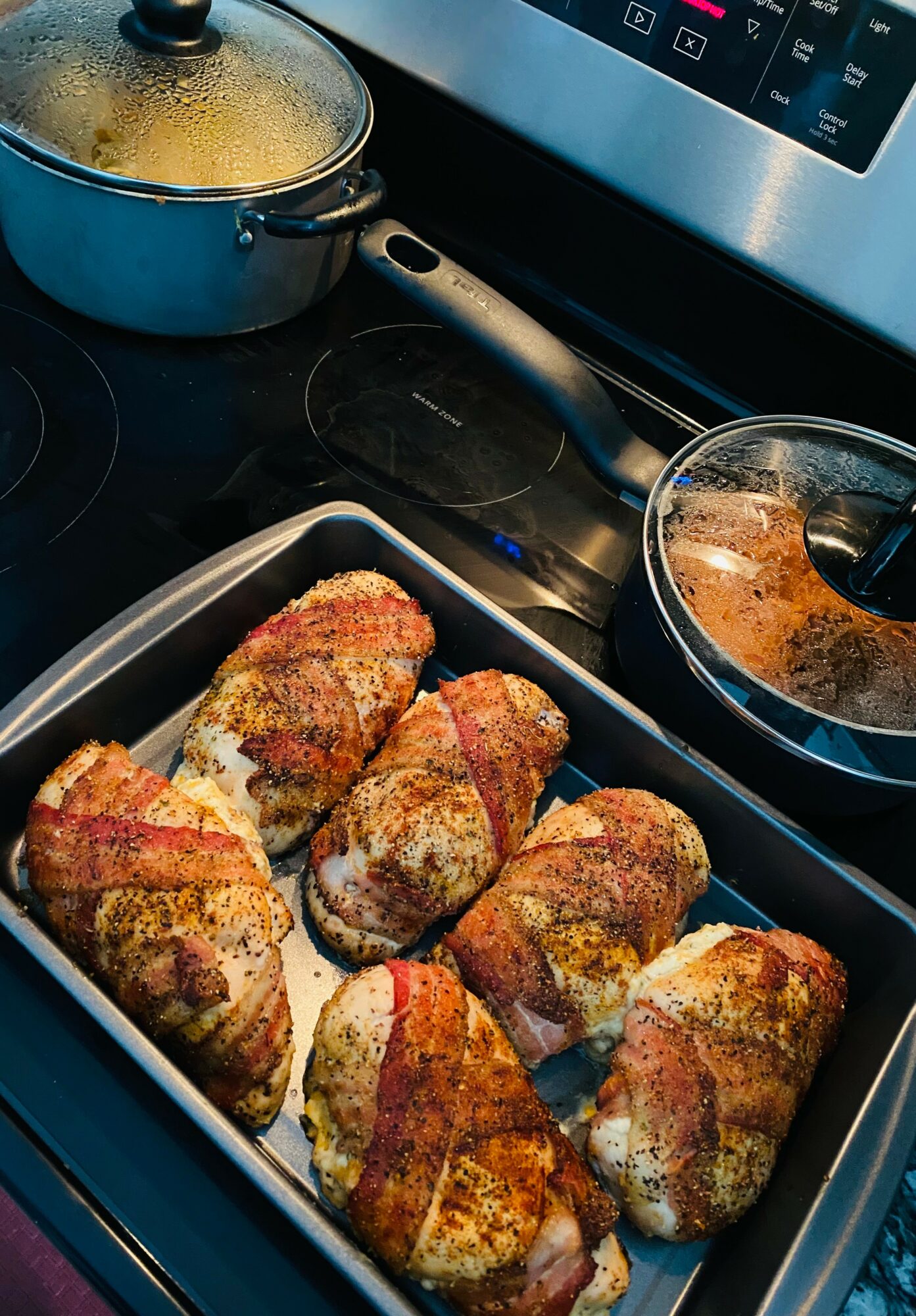 Baking dish with seven breaded, cooked chicken pieces on a stovetop, with pots and a pan nearby.